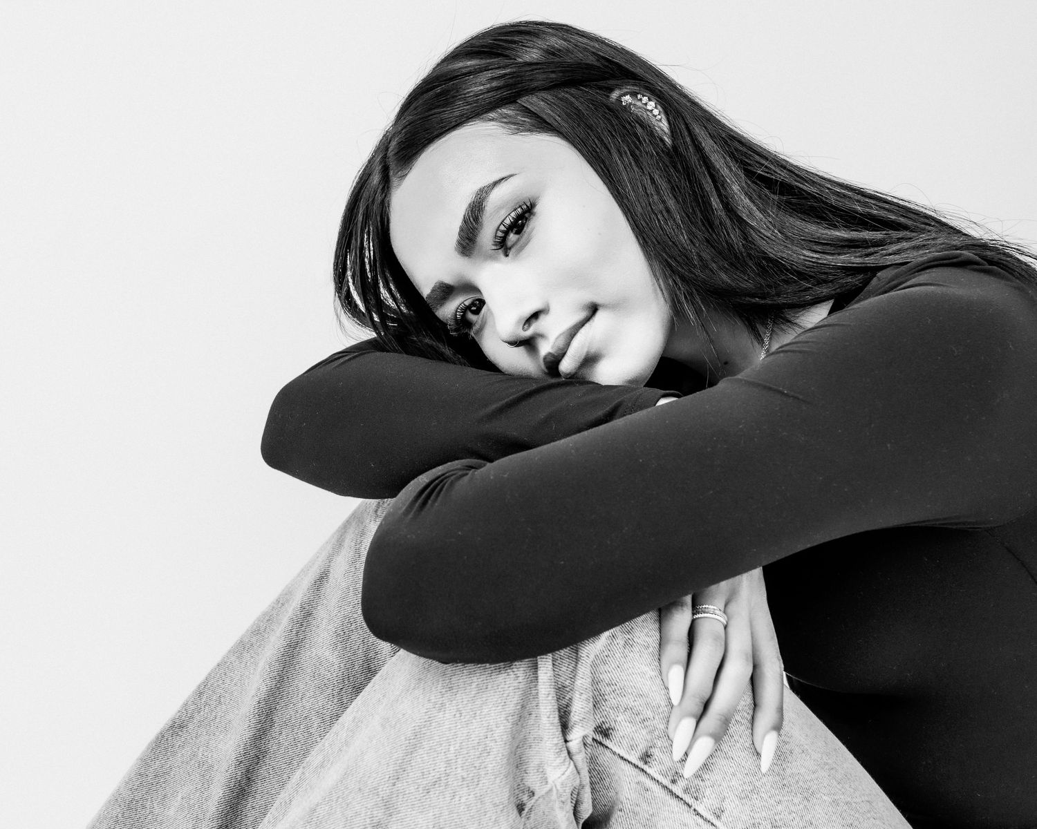 Black and white portrait of a young woman with long dark hair resting her chin on her arms.