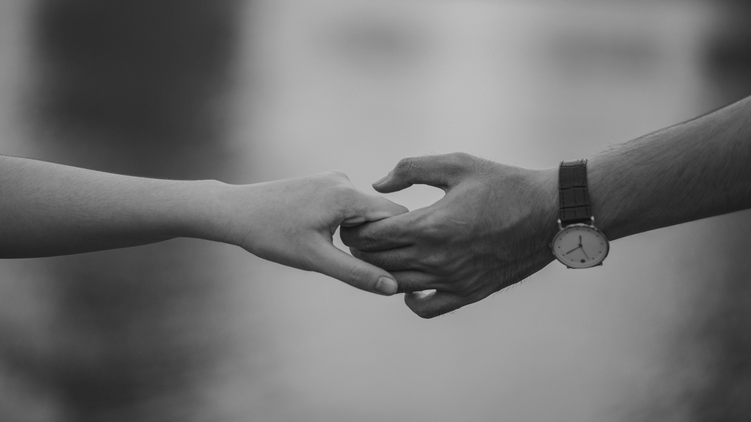 Black and white close-up of two people holding hands, one wearing a classic wristwatch.