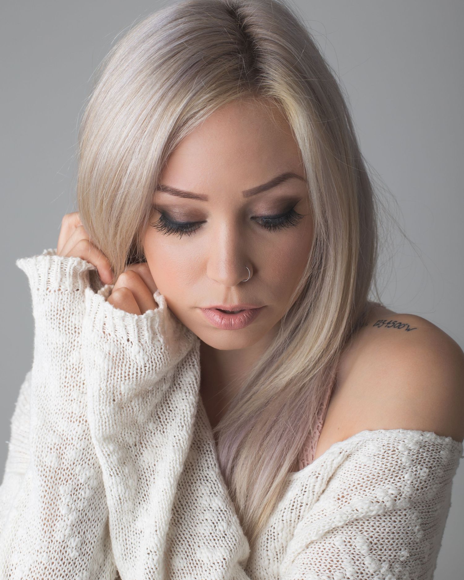 Blonde woman in off-shoulder white sweater with tattoo posing in a professional studio portrait.