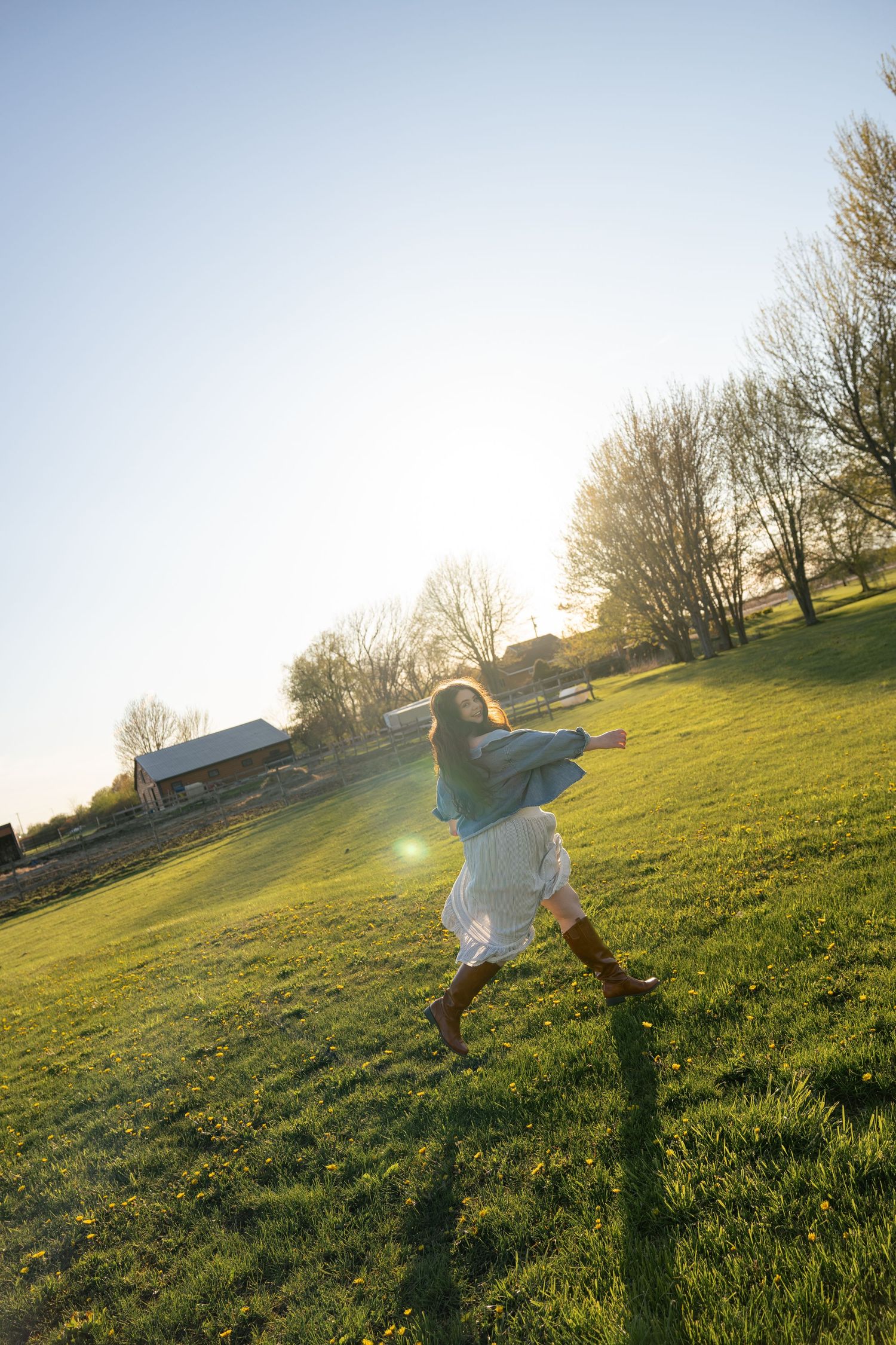Woman in denim jacket and white skirt running through a sunlit green field with lens flare.