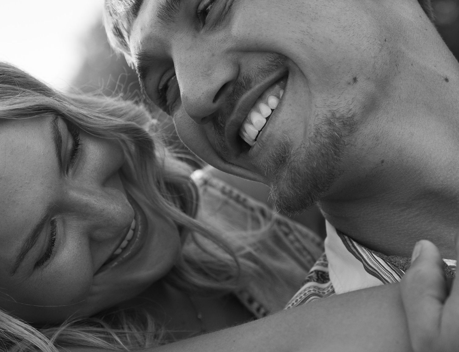 Black and white close-up of a laughing couple embracing and smiling together in a joyful candid moment.