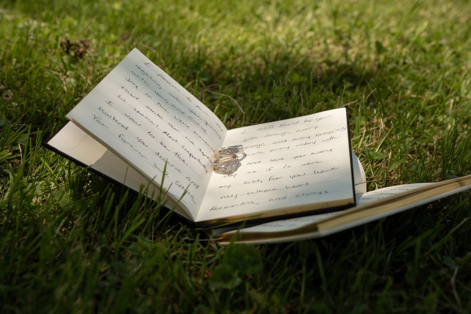 Open handwritten journal with a ring resting on its pages lying on lush green grass.