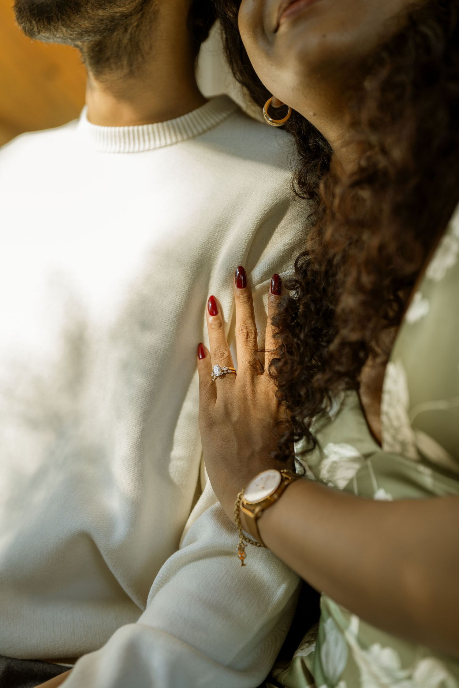 Close-up of couple embracing, woman with curly hair and red nails resting hand on mans white sweater.