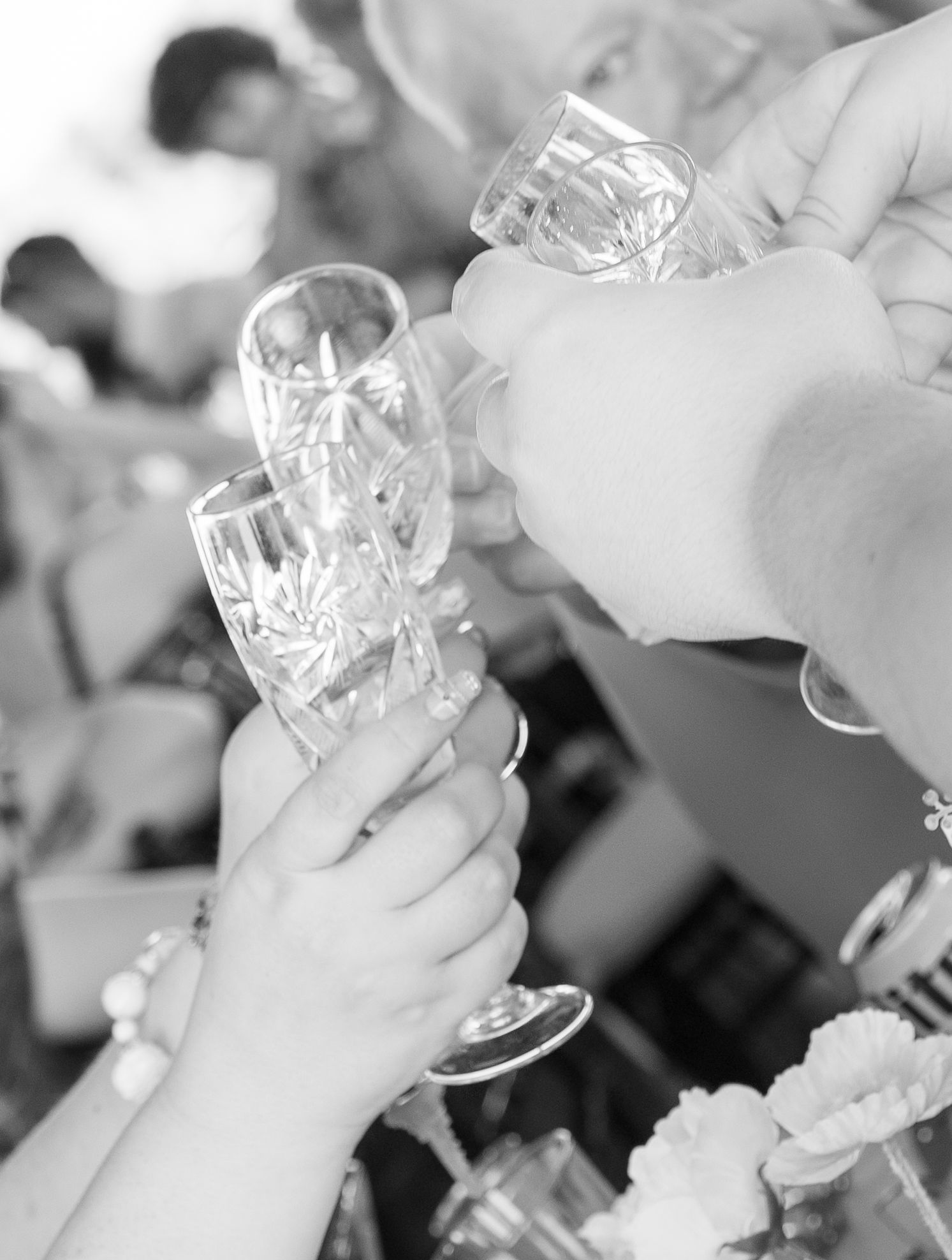 Black and white photo of hands clinking crystal champagne glasses at wedding celebration toast.