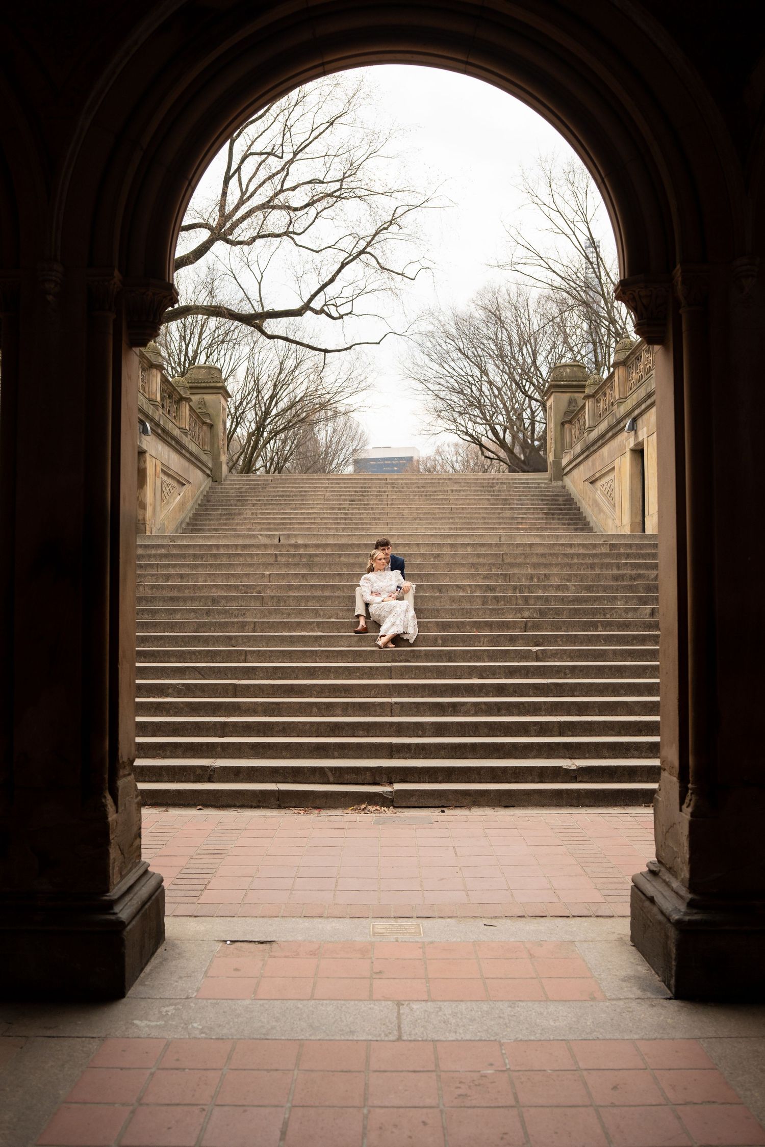 Couple sitting together on grand stone steps viewed through an arched tunnel in Central Park, New York.