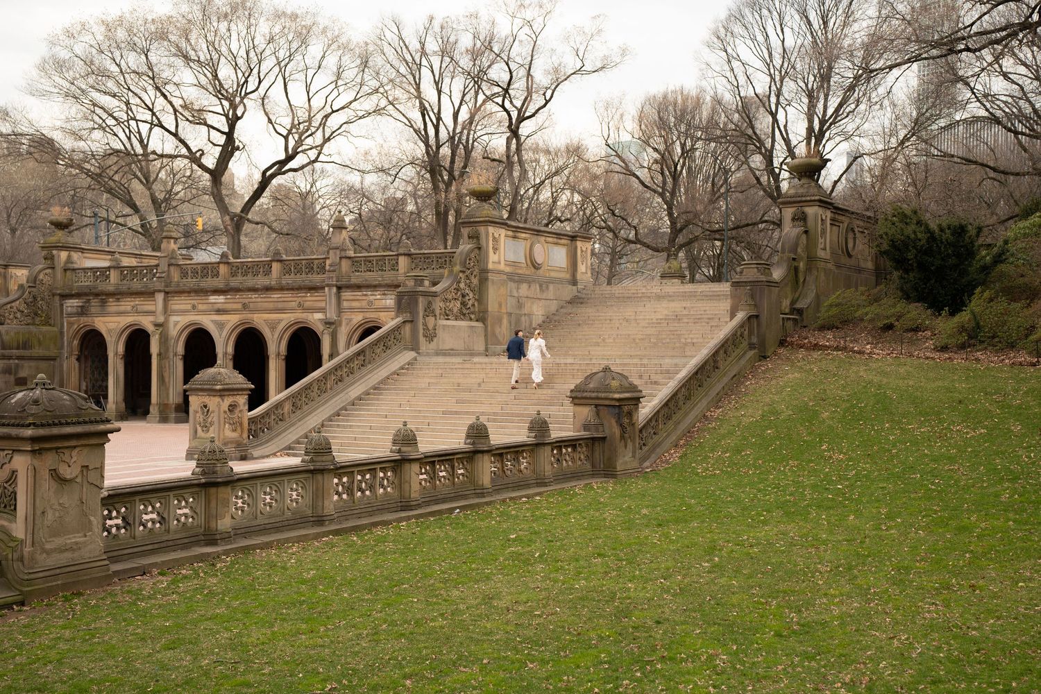 Couple in wedding attire walking along a stone balustrade staircase at Bethesda Terrace in Central Park.