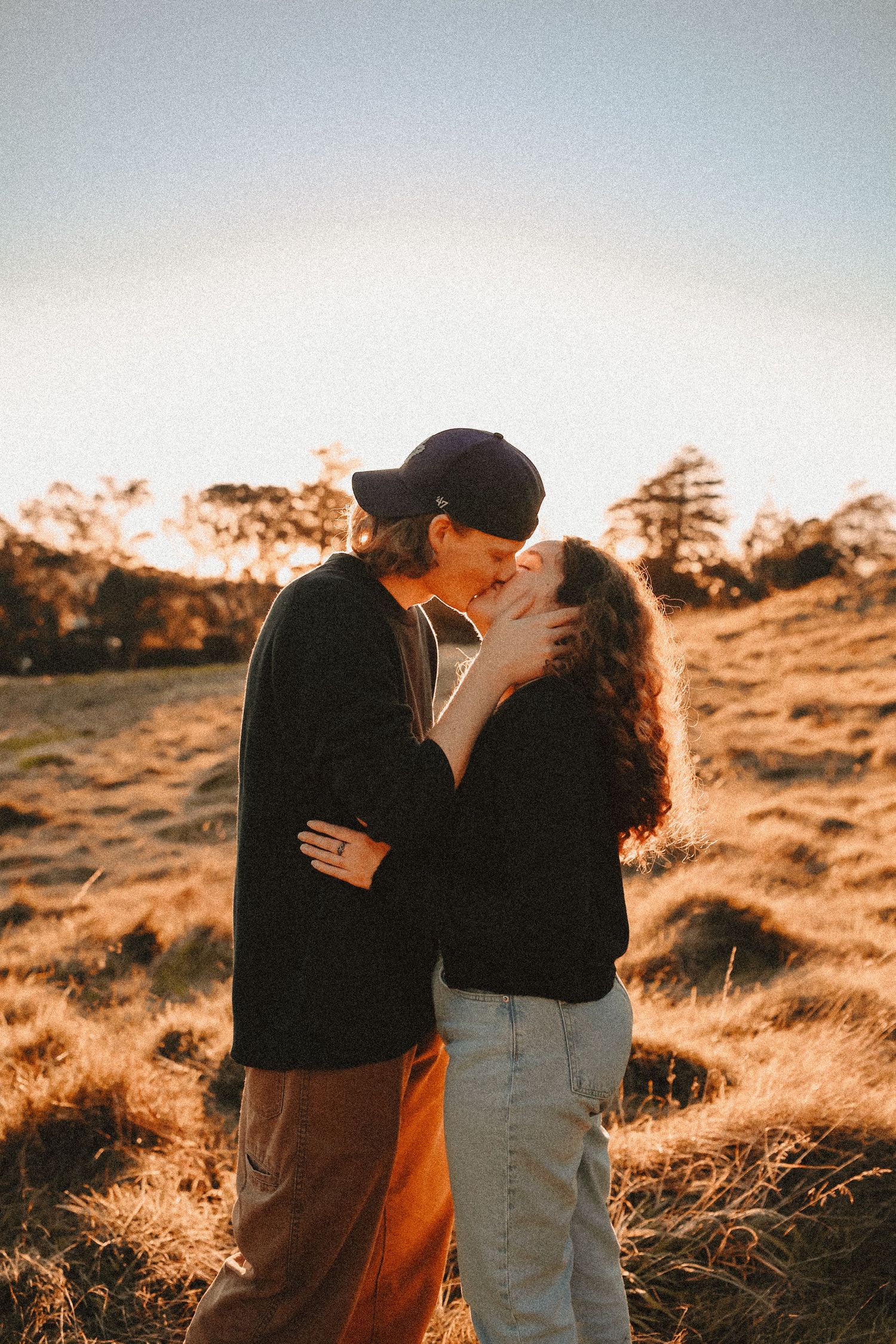 A couple enjoying a golden hour stroll through an open field with backlit sunset flare.