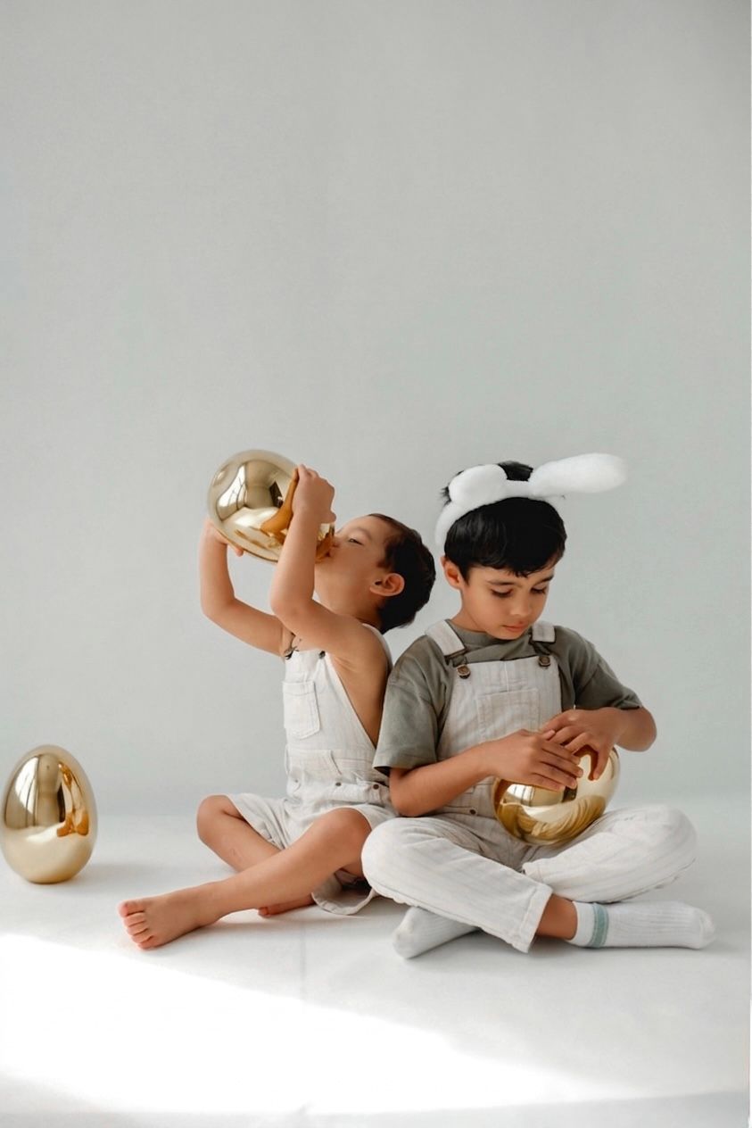 Action shot of siblings looking for colorful Easter eggs in a decorated studio set.