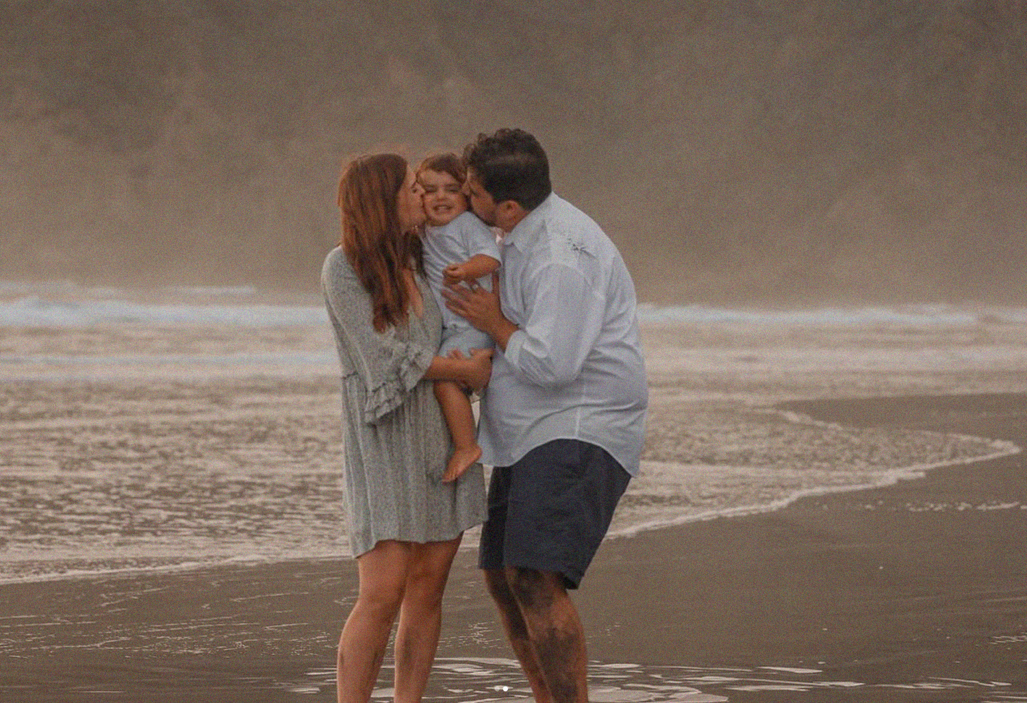 Candid moment of a father lifting his toddler in the air during a sunset beach photoshoot.