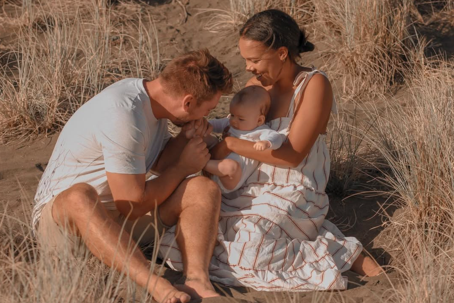 Family session at Piha Beach in the dunes. dad kissing the baby tiny toes.
