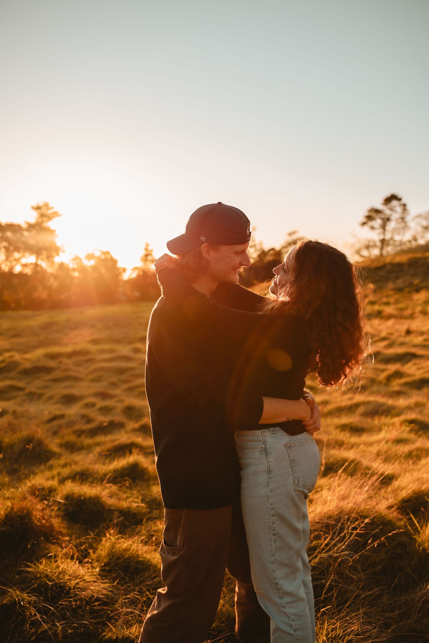 A close-up of a couple embracing in a tall grass meadow during a vibrant summer sunset.