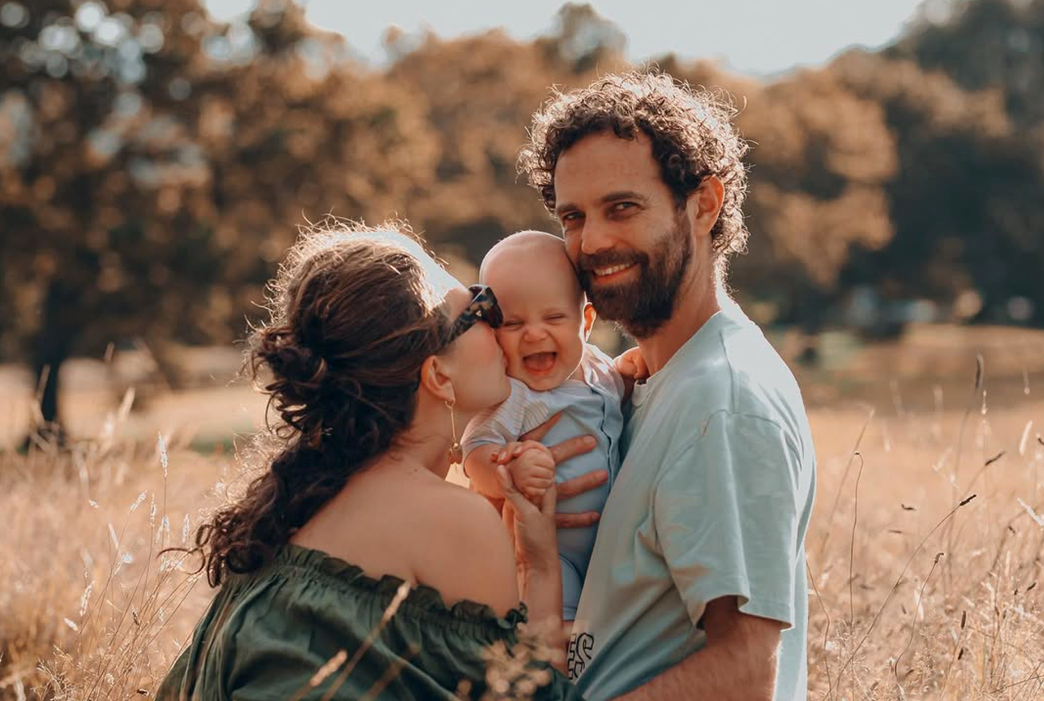 Candid family portrait under the large oak trees at Cornwall Park, Auckland, during a golden hour session.