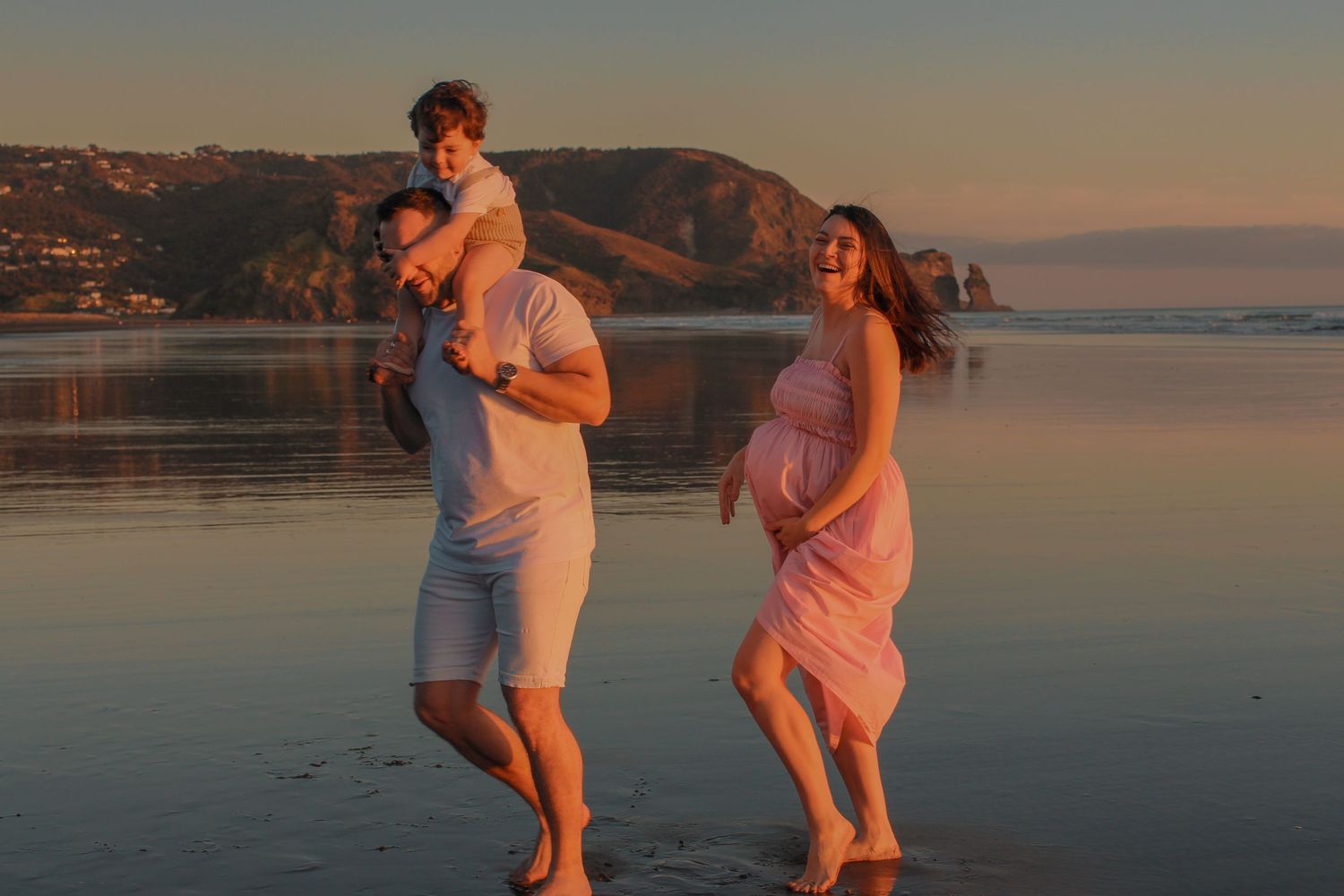 Maternity Photographer based in Auckland. Photographing during golden hour.  Photos taken at Piha Beach, with laughs.