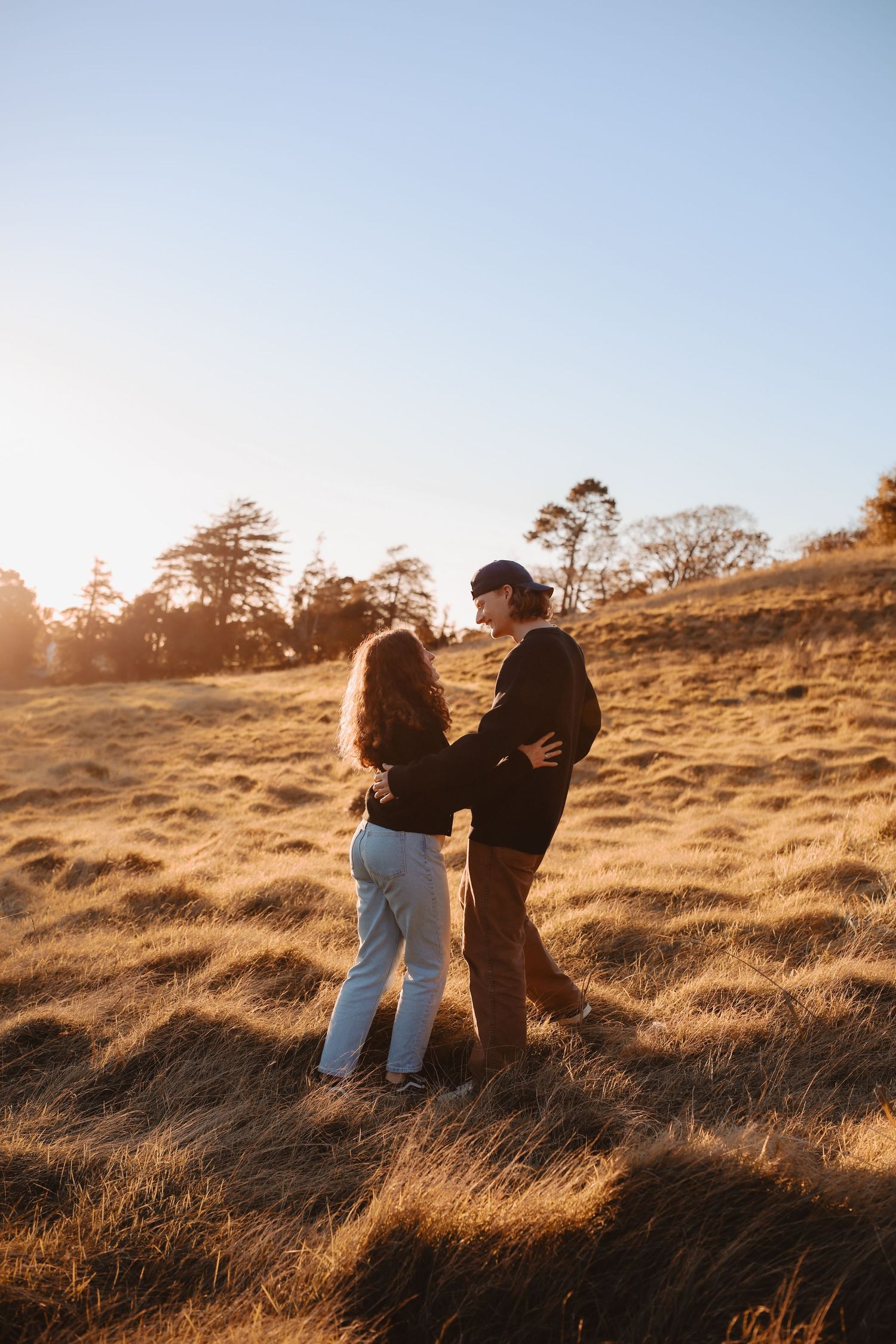 A tight focus on a couple's faces as they stand close together, backlit by the warm evening sun.