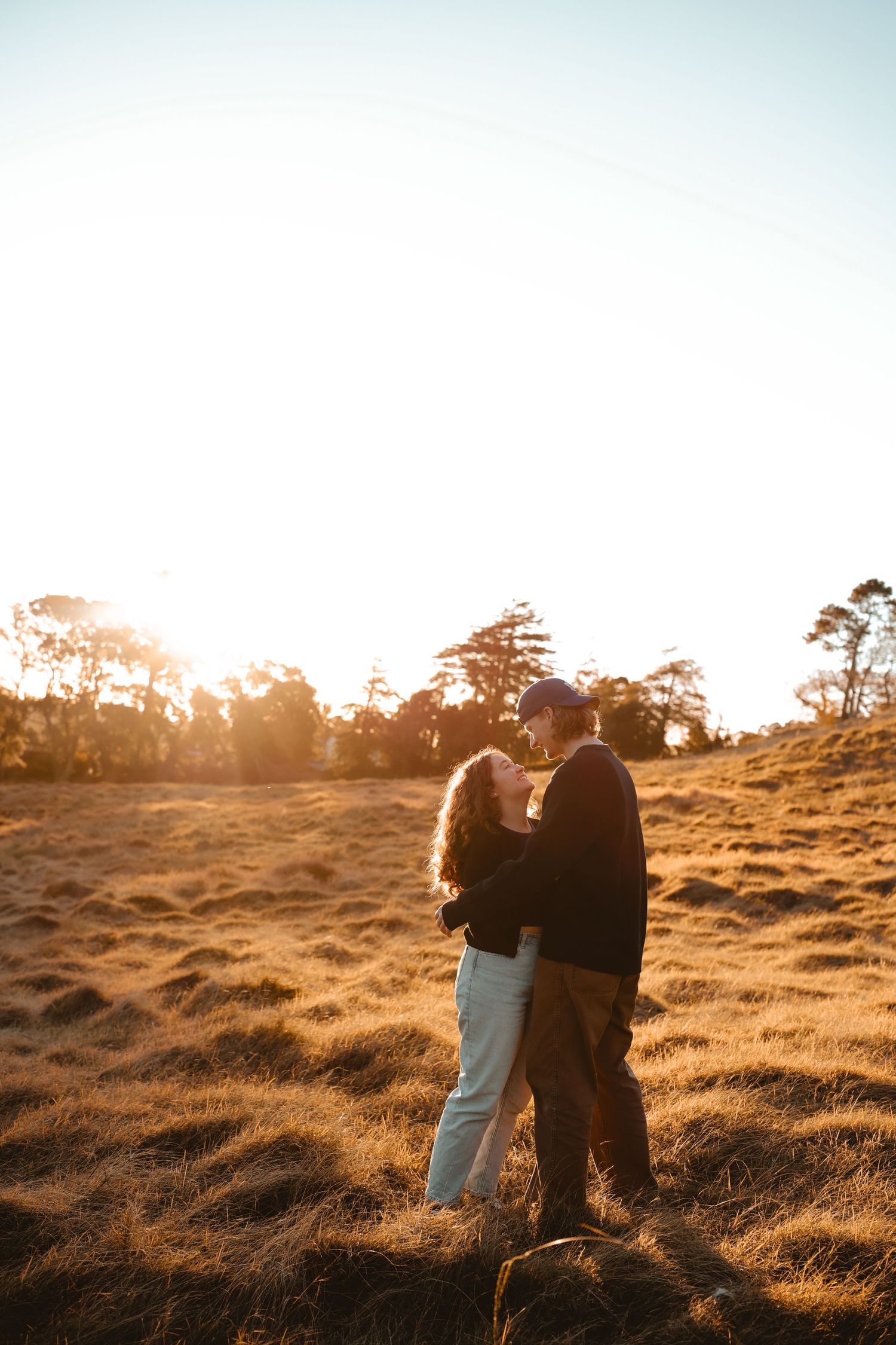 A peaceful moment between a couple with their eyes closed, hugging in a quiet field during twilight.