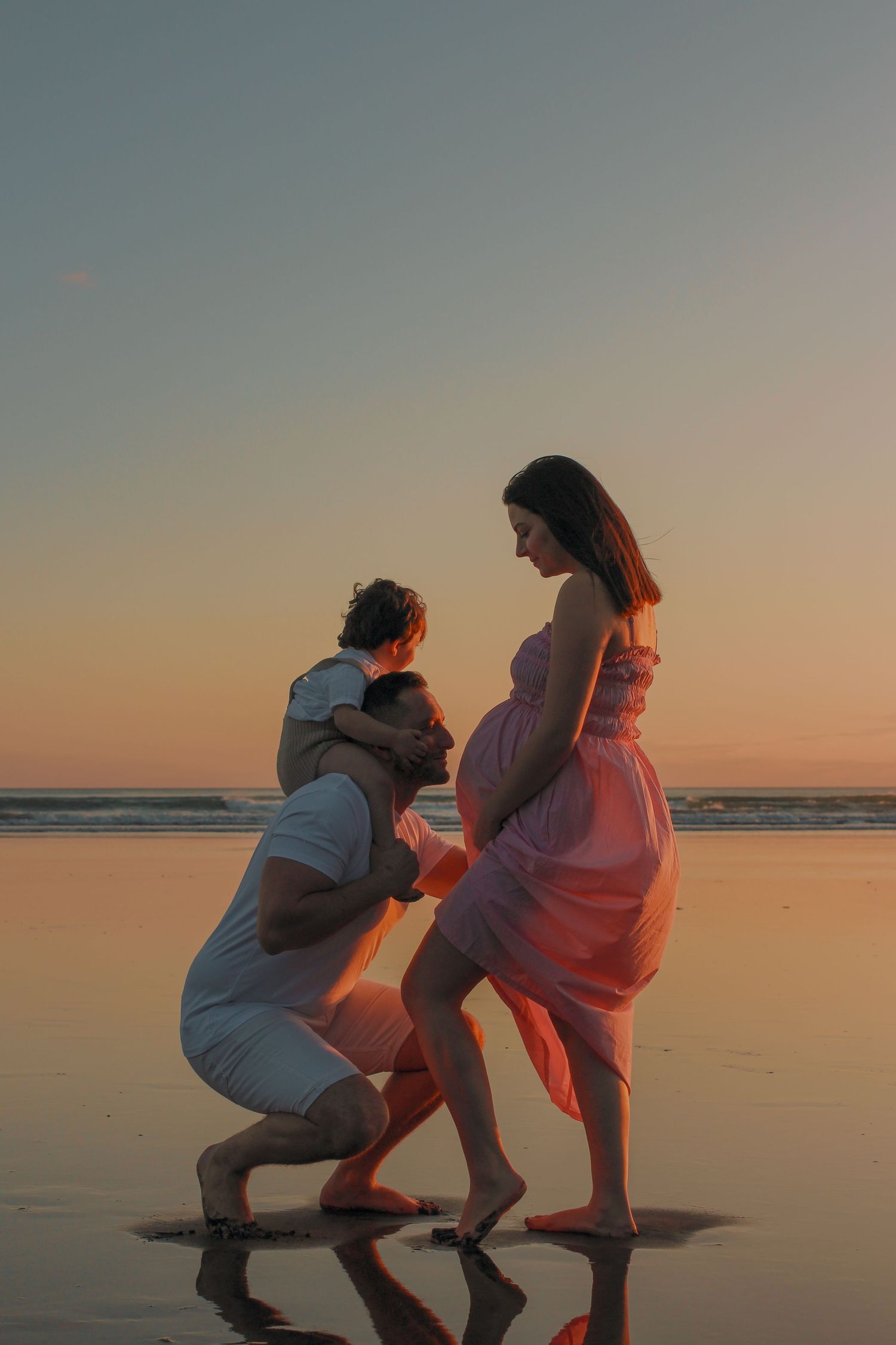 Maternity Photographer based in Auckland. Photographing during golden hour.  Photos taken at Piha Beach. Dad kissing pregnant  belly.