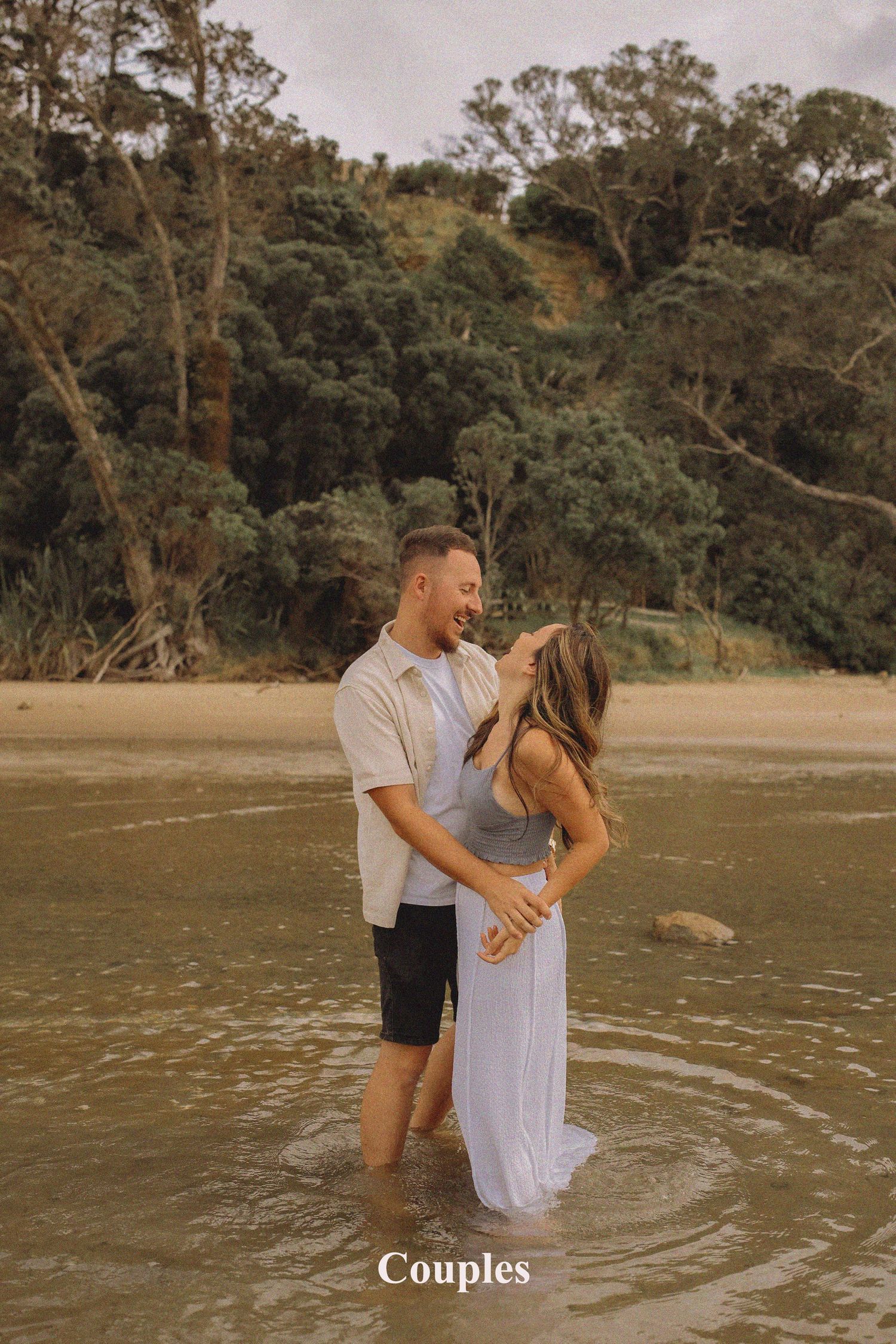 A couple walking hand-in-hand along the black sand shoreline at Long Bay Beach during a dramatic sunset session.