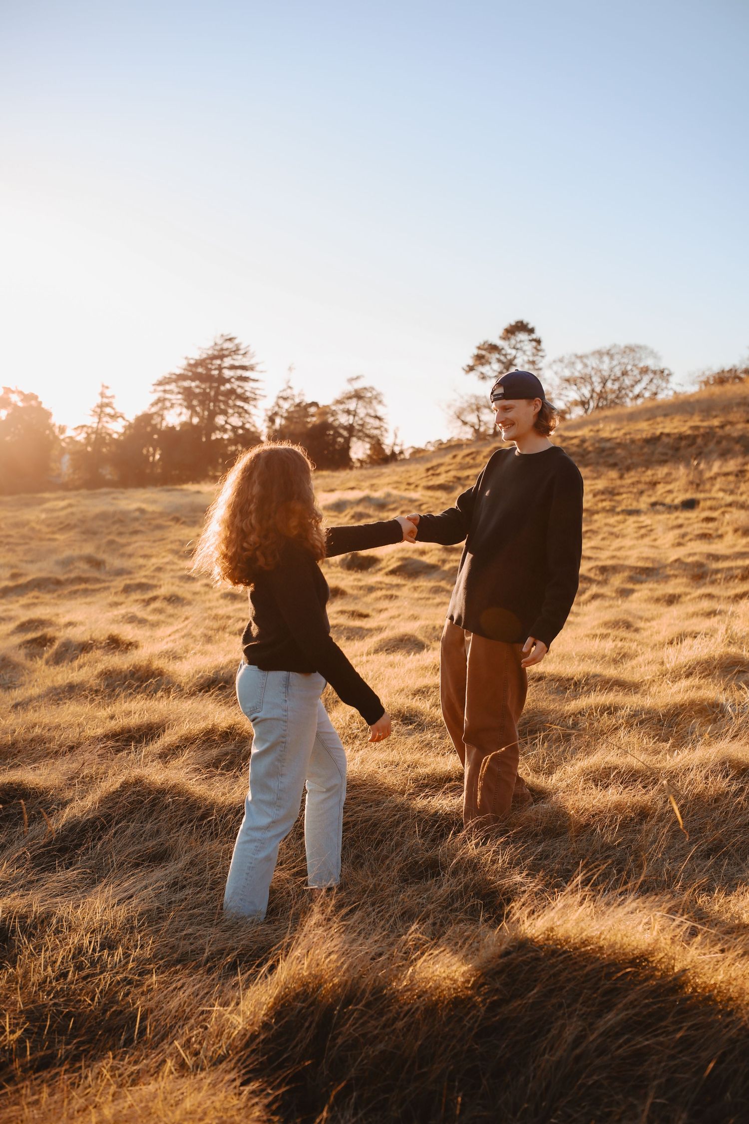 A young couple in trendy autumn wardrobe sharing an affectionate, unposed moment during an outdoor photoshoot.