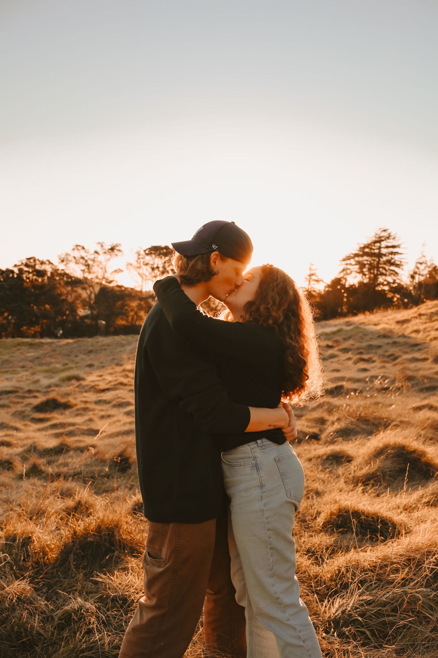 A man and woman in casual autumn attire dancing together in a rustic field at dusk.