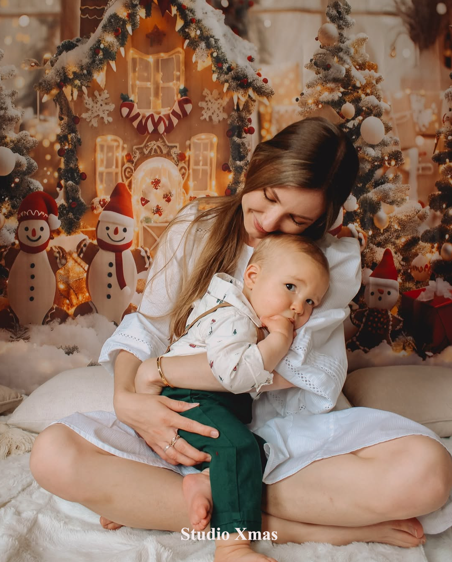 Festive Auckland studio photography session featuring a mother and child posing in front of a Christmas gingerbread house backdrop.