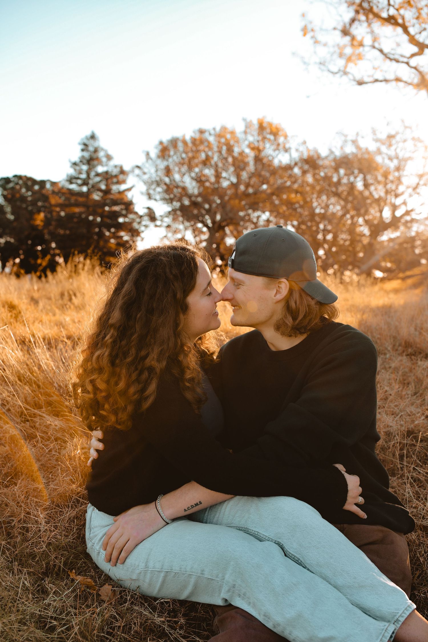 A high-end lifestyle portrait capturing a romantic couple sharing an intimate whisper in a sunset meadow.