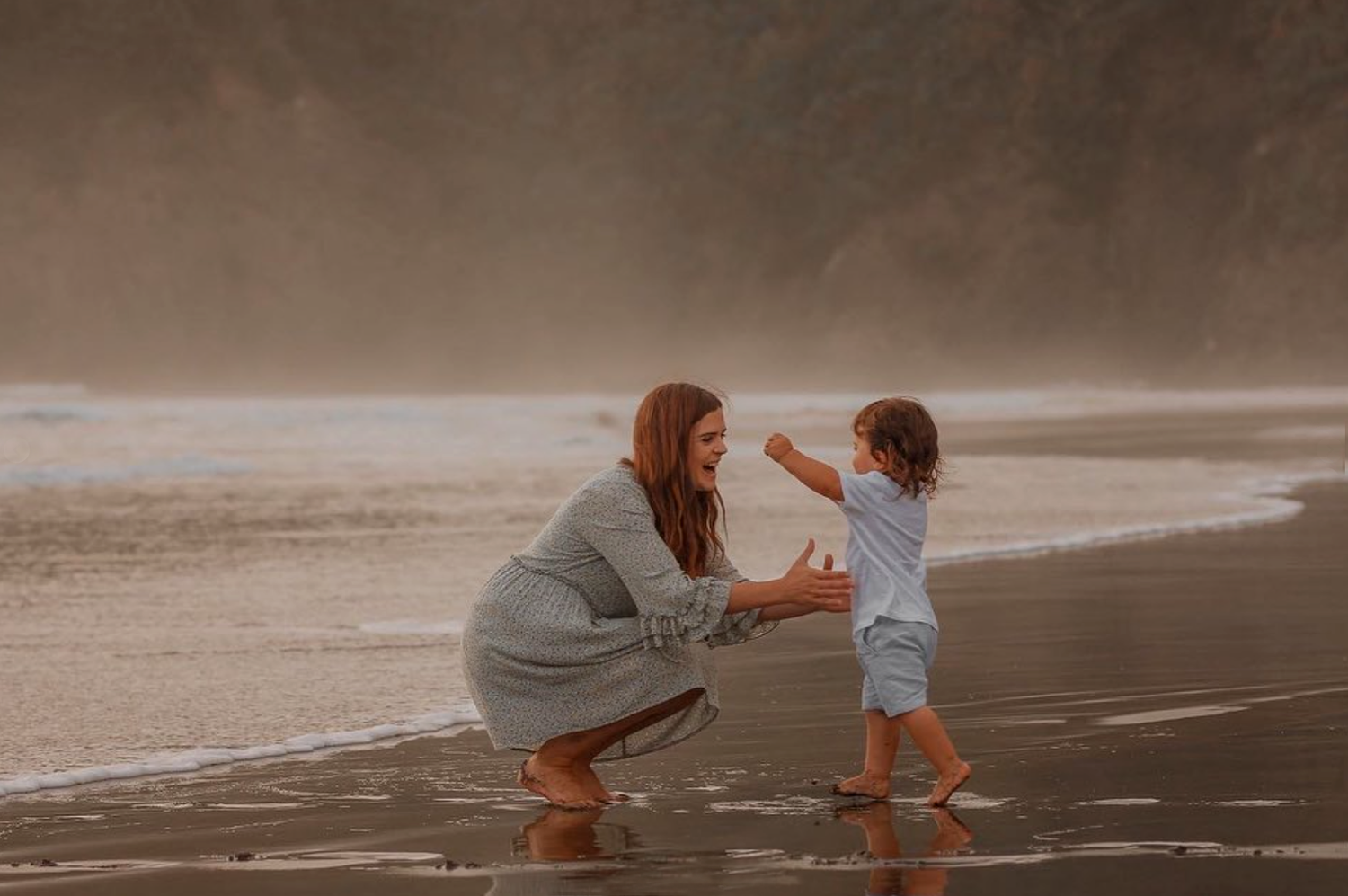 Dramatic maternity session at Piha Beach featuring the black sand and Lion Rock in the background.