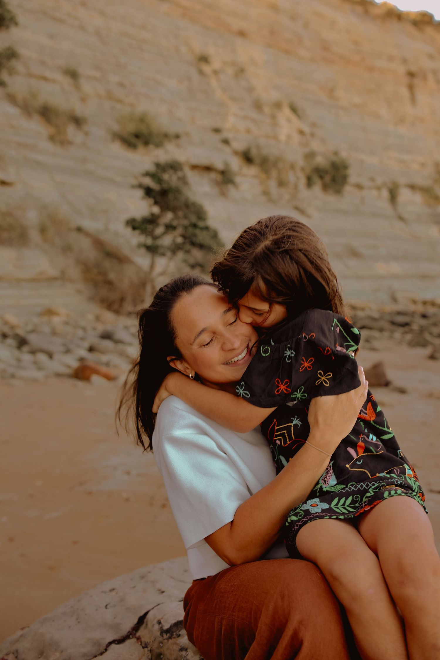 Family Photographer based in Auckland. Mother and daughter sitting on rock at Long Bay Beach