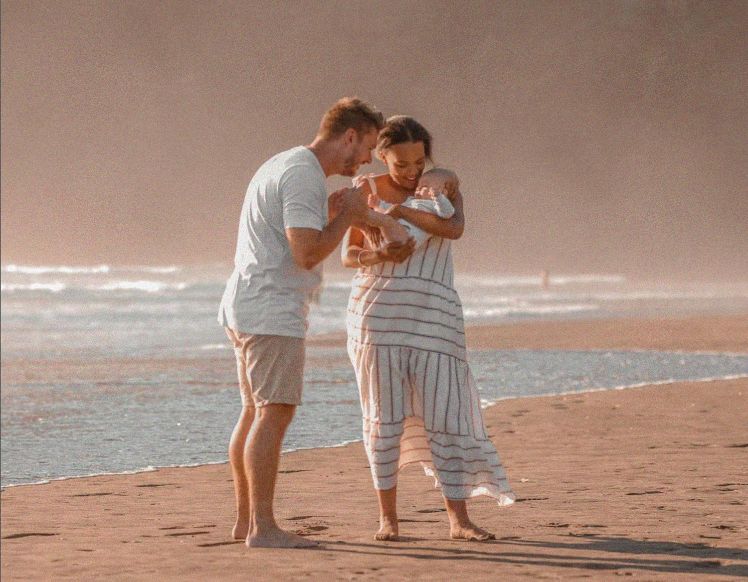 Family Photographer based in Auckland, with baby held by mum as dad kisses tiny feet.