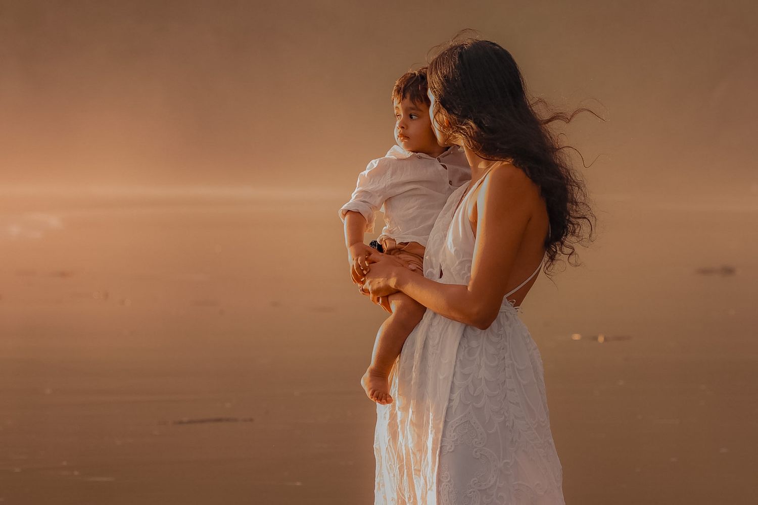 Mum carrying her child during sunset.  photo during golden hour at piha amongst the mist.