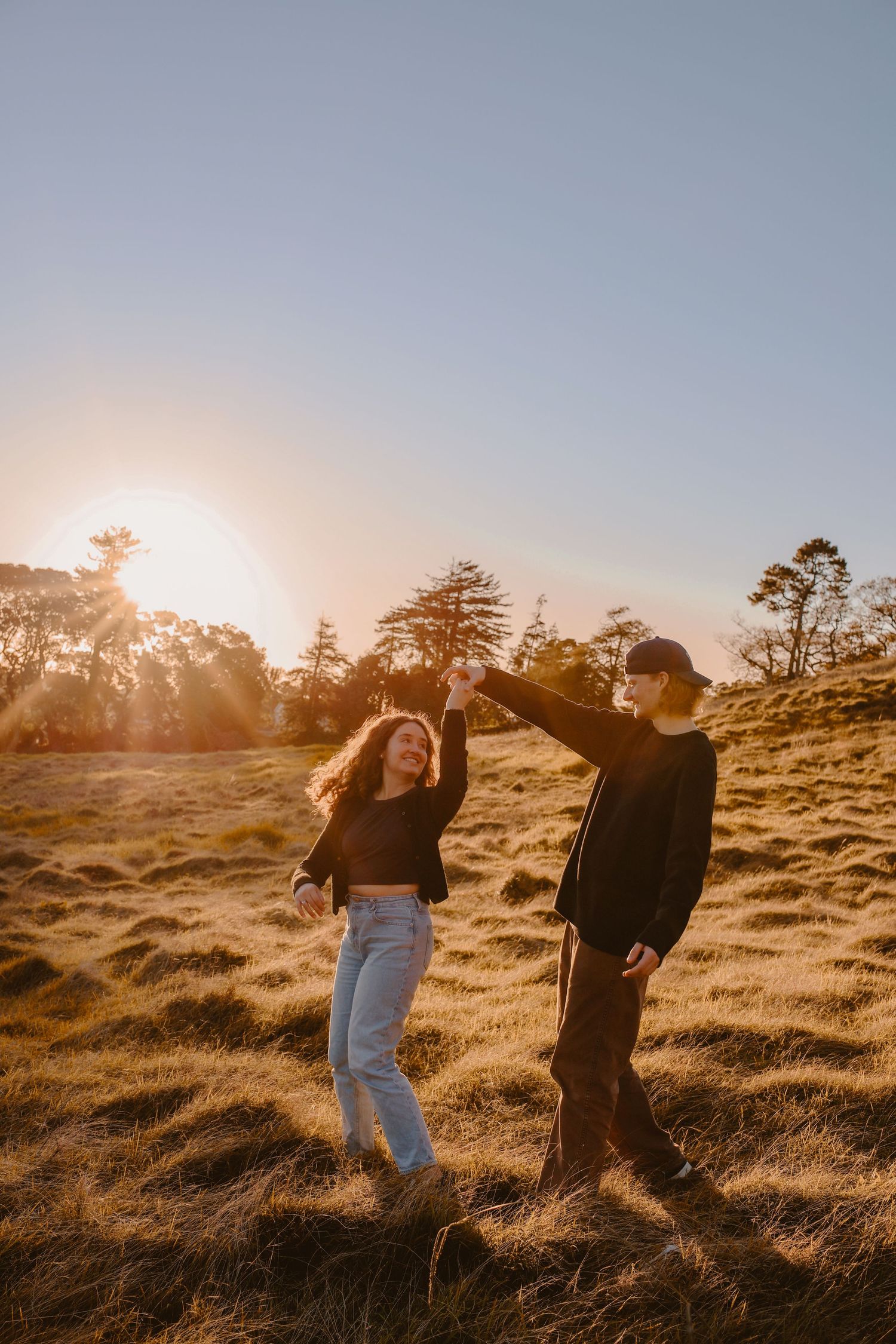 Side profile of a couple sharing a private laugh and looking at each other lovingly in a sunlit field.