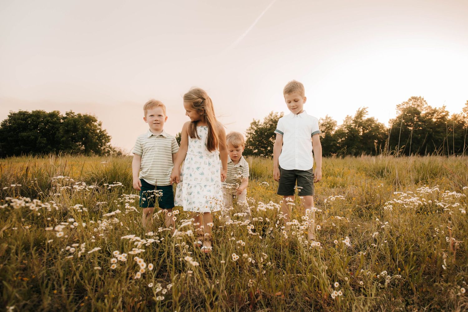 Three children standing in a wildflower meadow at sunset.
