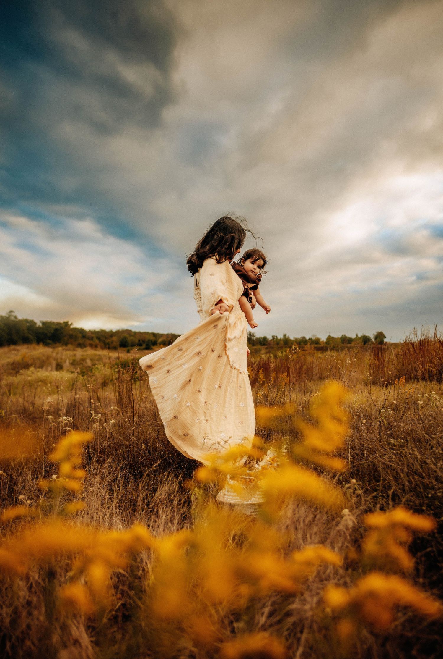 Flowing white dress twirls through tall grass under dramatic cloudy sky.