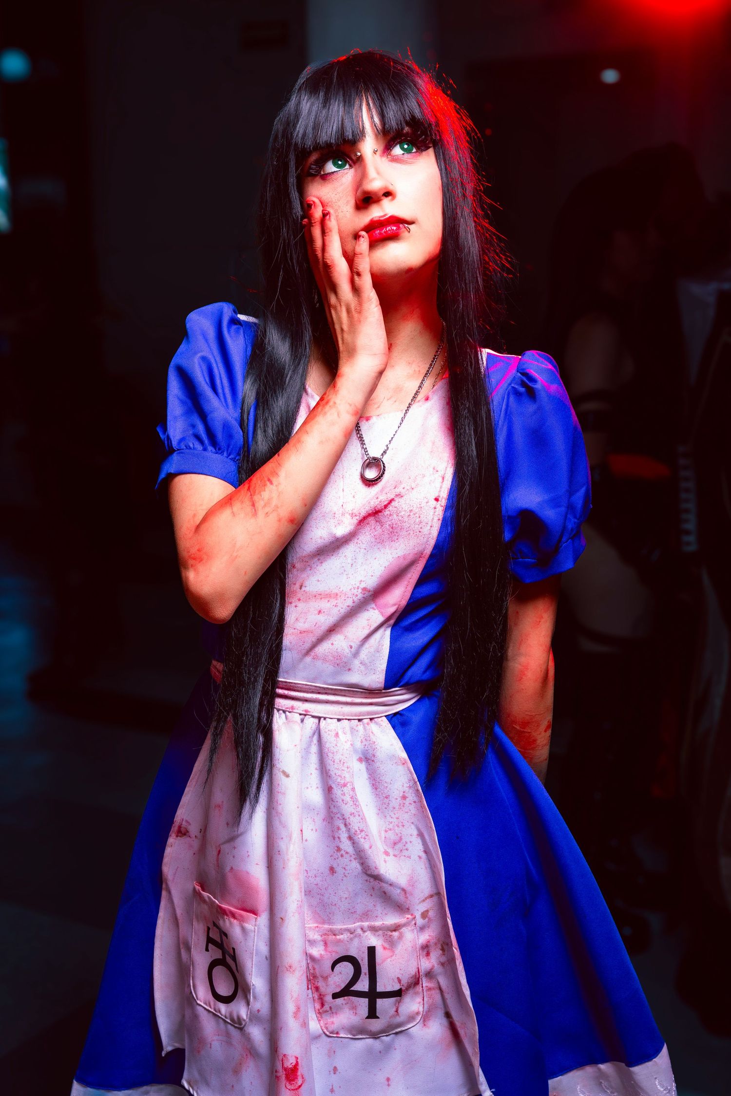 A figure in a blue dress with puffy sleeves and a white blood-stained apron poses dramatically in a dark setting.
