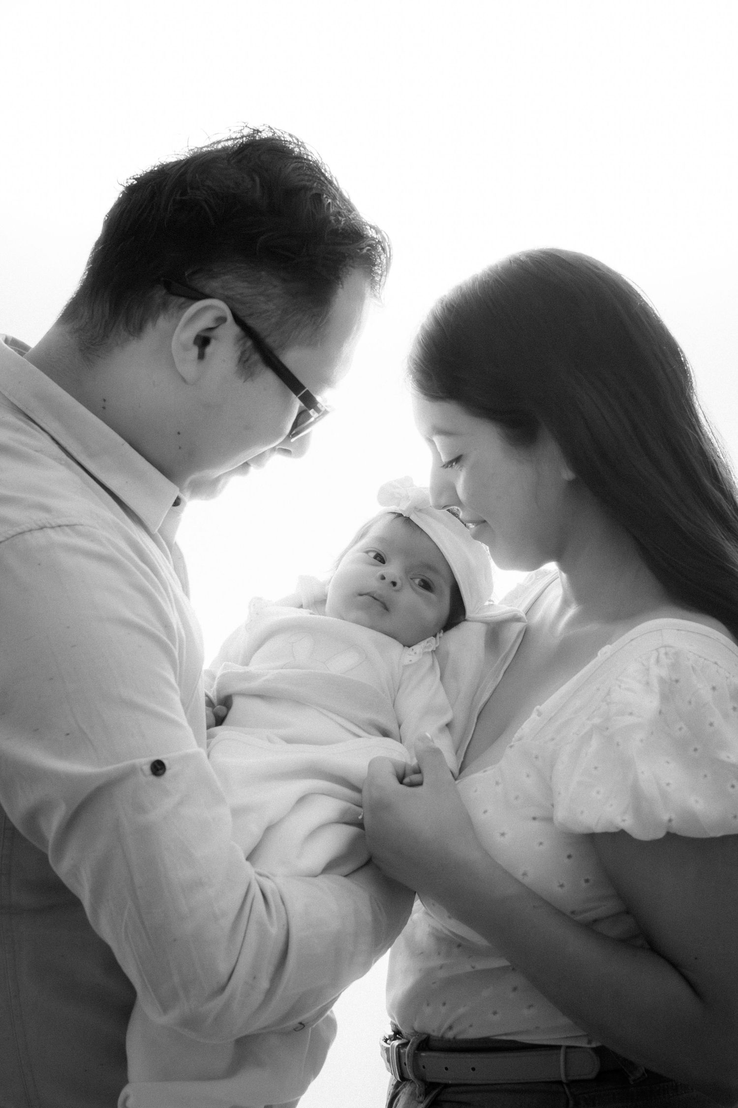 Black and white intimate family portrait of parents holding their newborn baby.