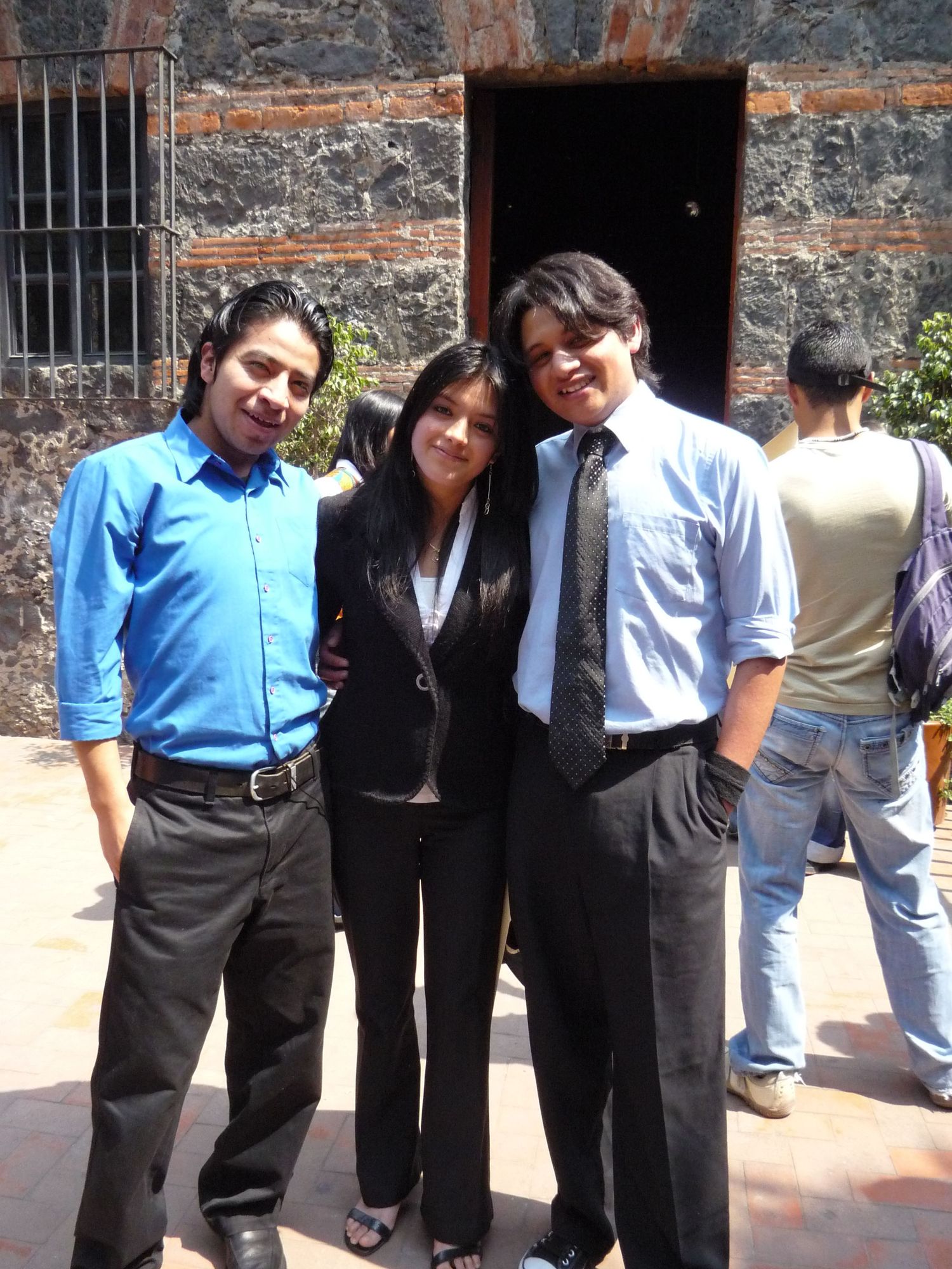 Three people dressed in business attire stand together outside a stone building.