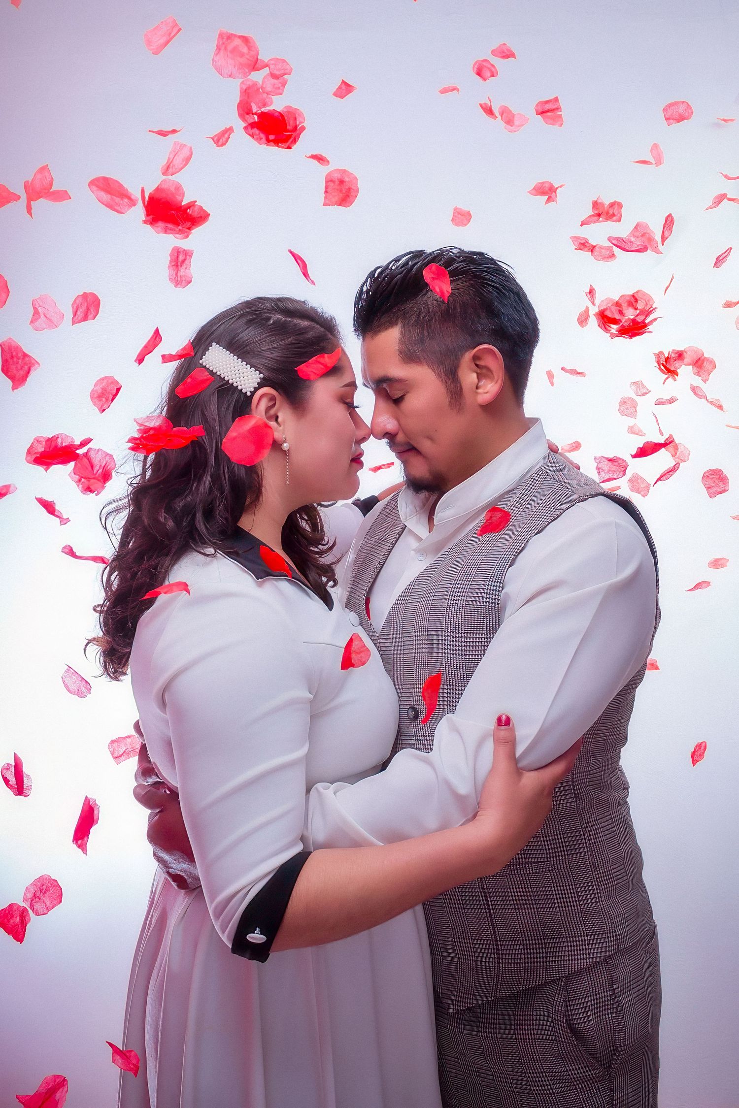 Romantic couple posing with floating red petals in studio setting.