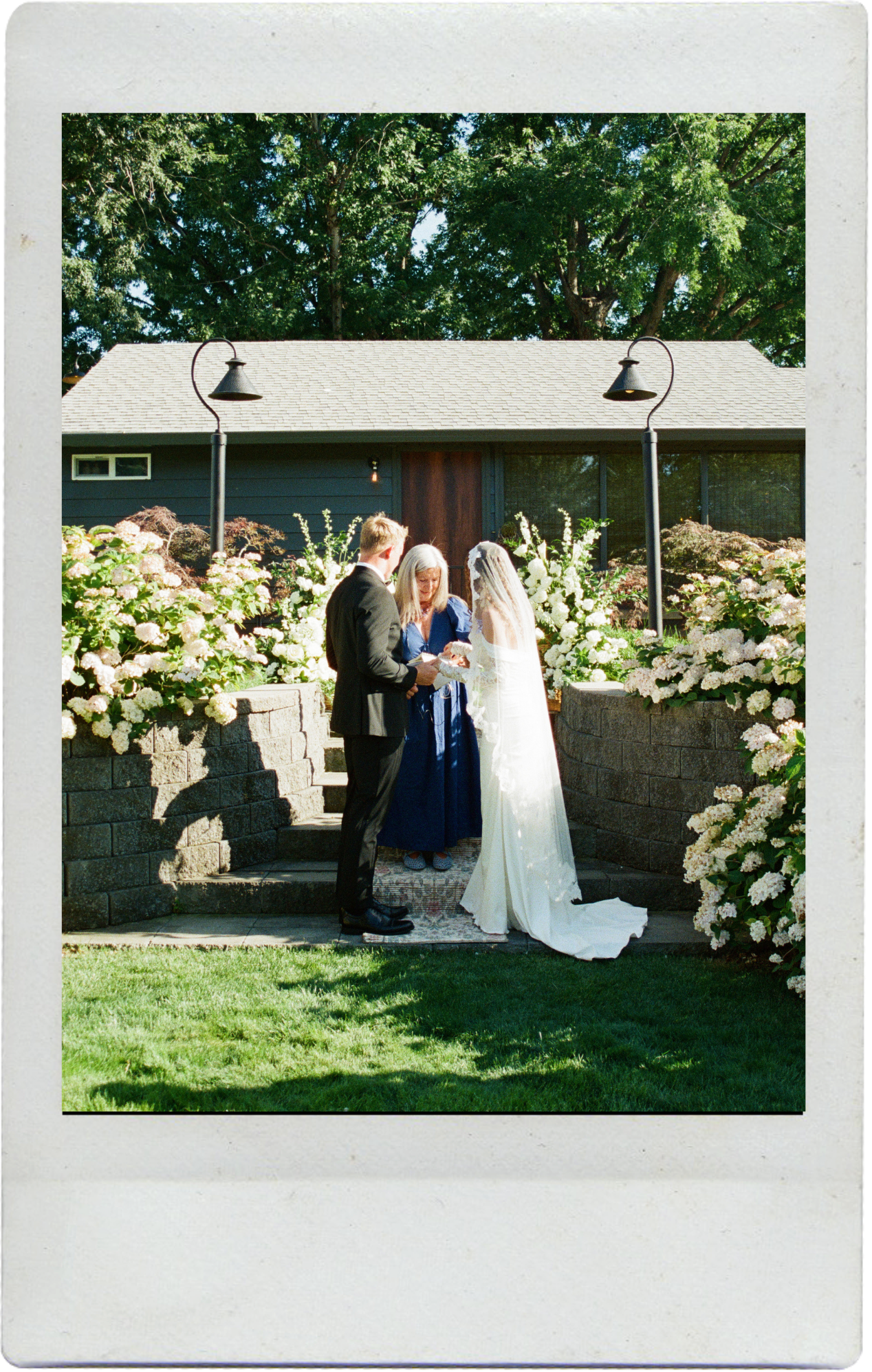 Outdoor garden wedding ceremony setup with white hydrangea flowers and decorative stone wall backdrop in sunlit setting.