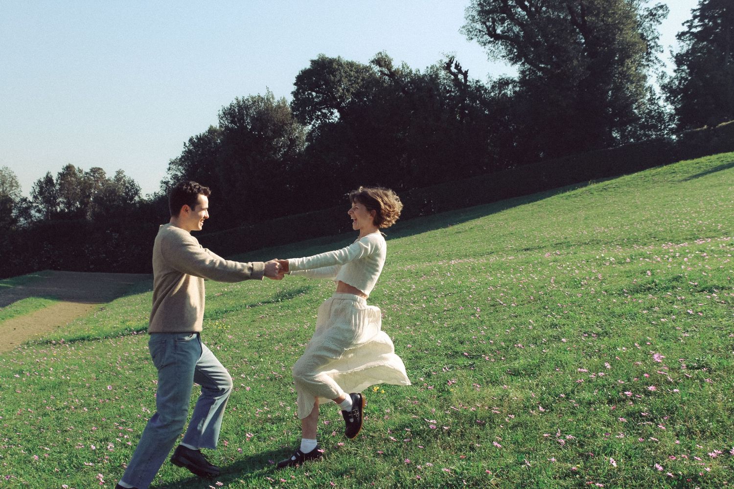 A couple dances playfully together in a grassy field on a sunny day.