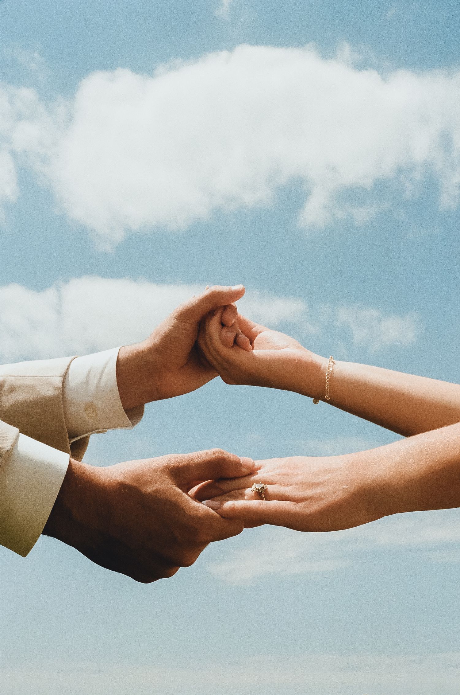 Close-up of hands joining together against blue cloudy sky.