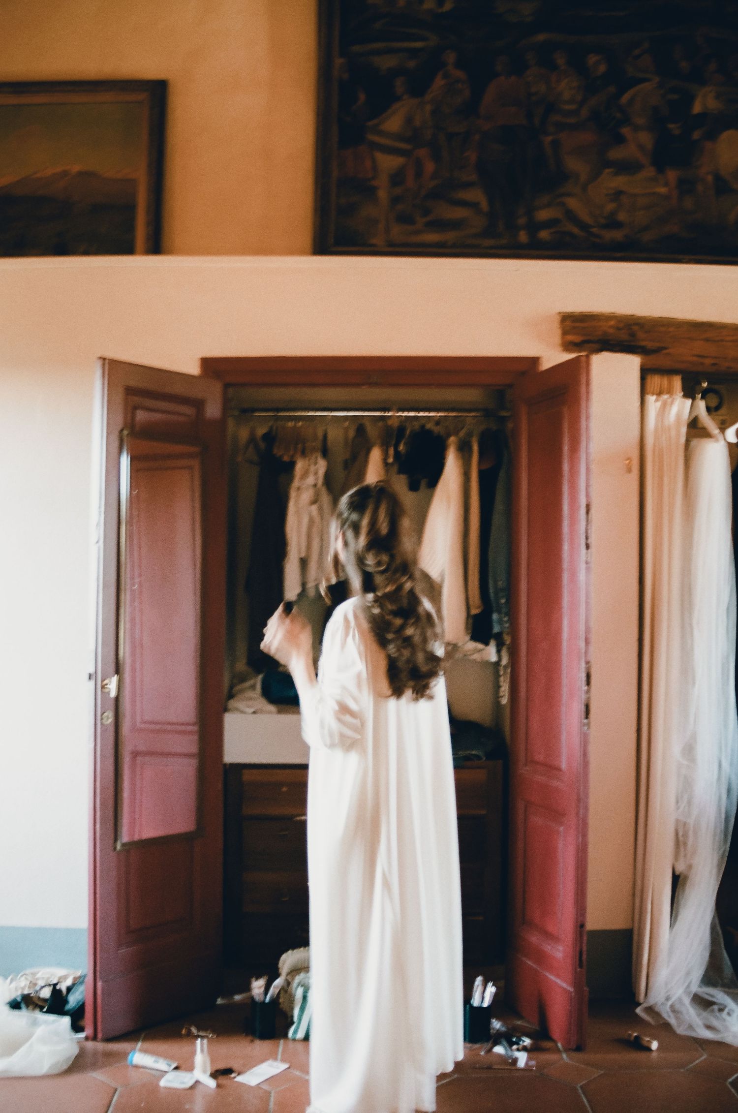 A wedding dress hangs elegantly on a wooden wardrobe door in a rustic room with warm lighting.