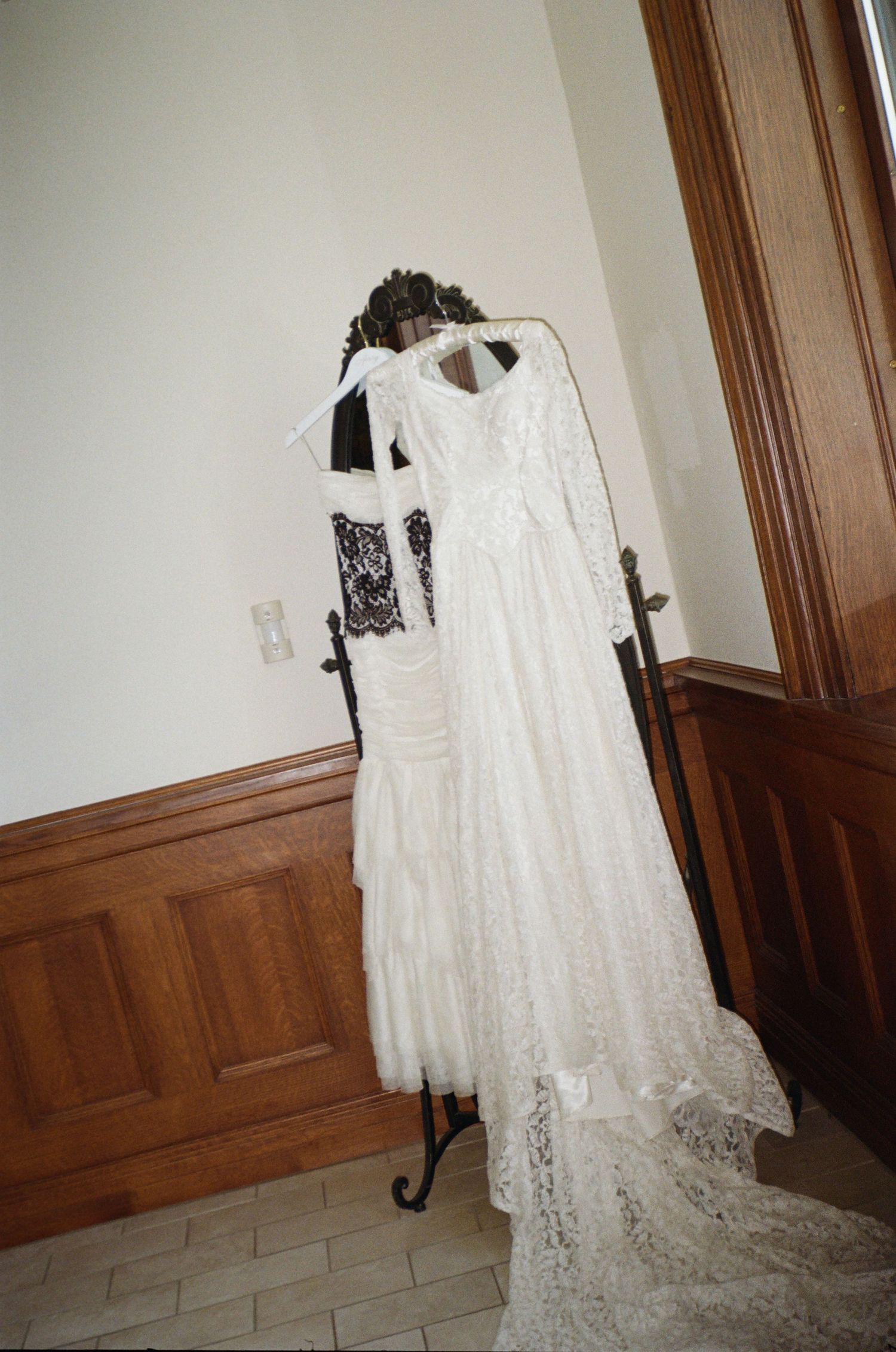 A white lace wedding dress displayed in sequence against a wooden wall with cream colored paint.