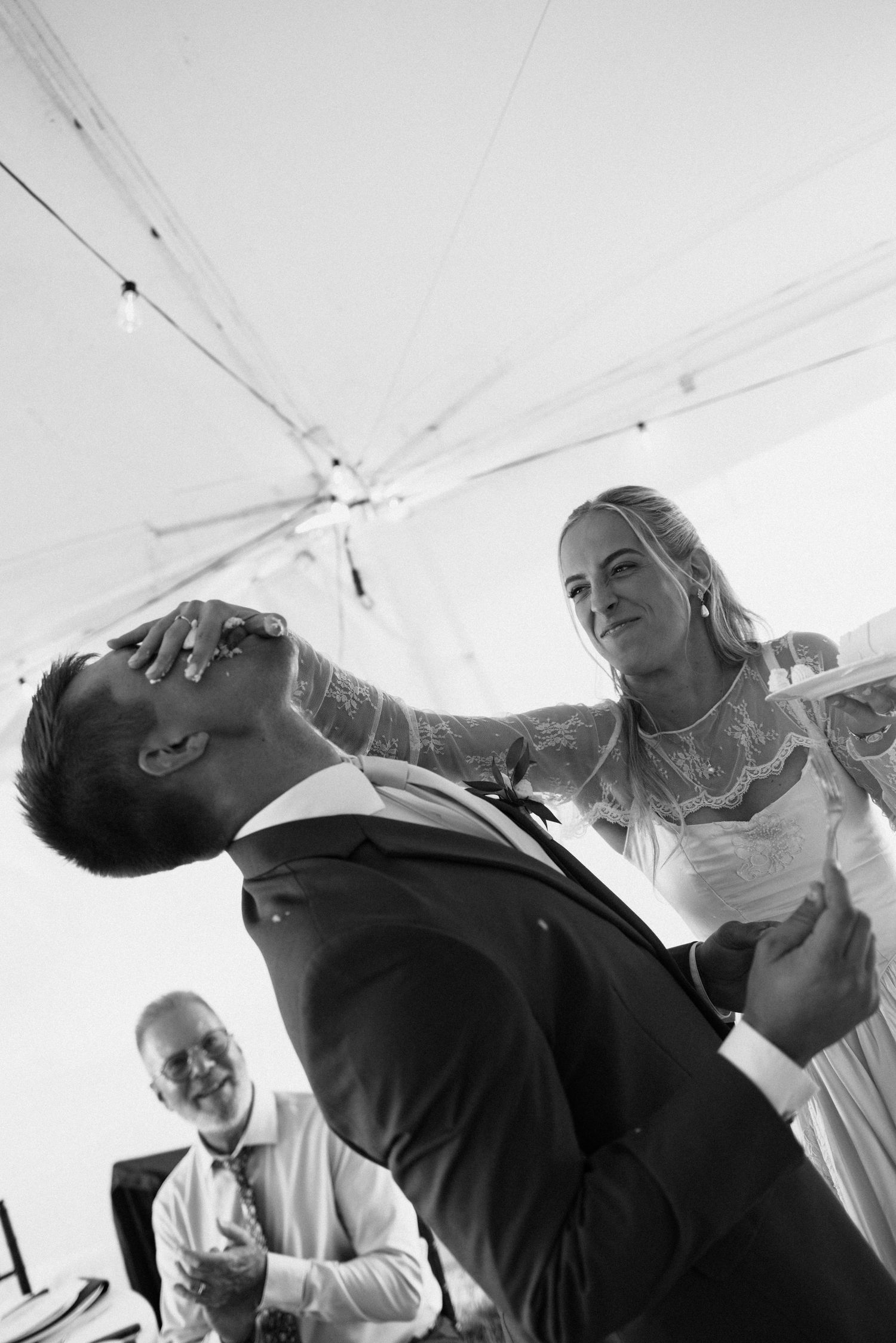 Black and white photo of a couple sharing a playful moment during their wedding reception under a tent.