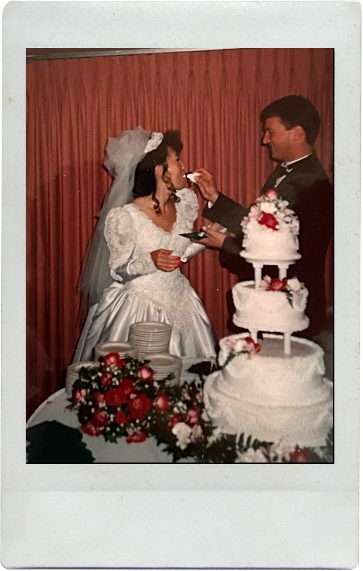 A traditional wedding cake cutting ceremony with a three-tiered white cake decorated with red flowers.