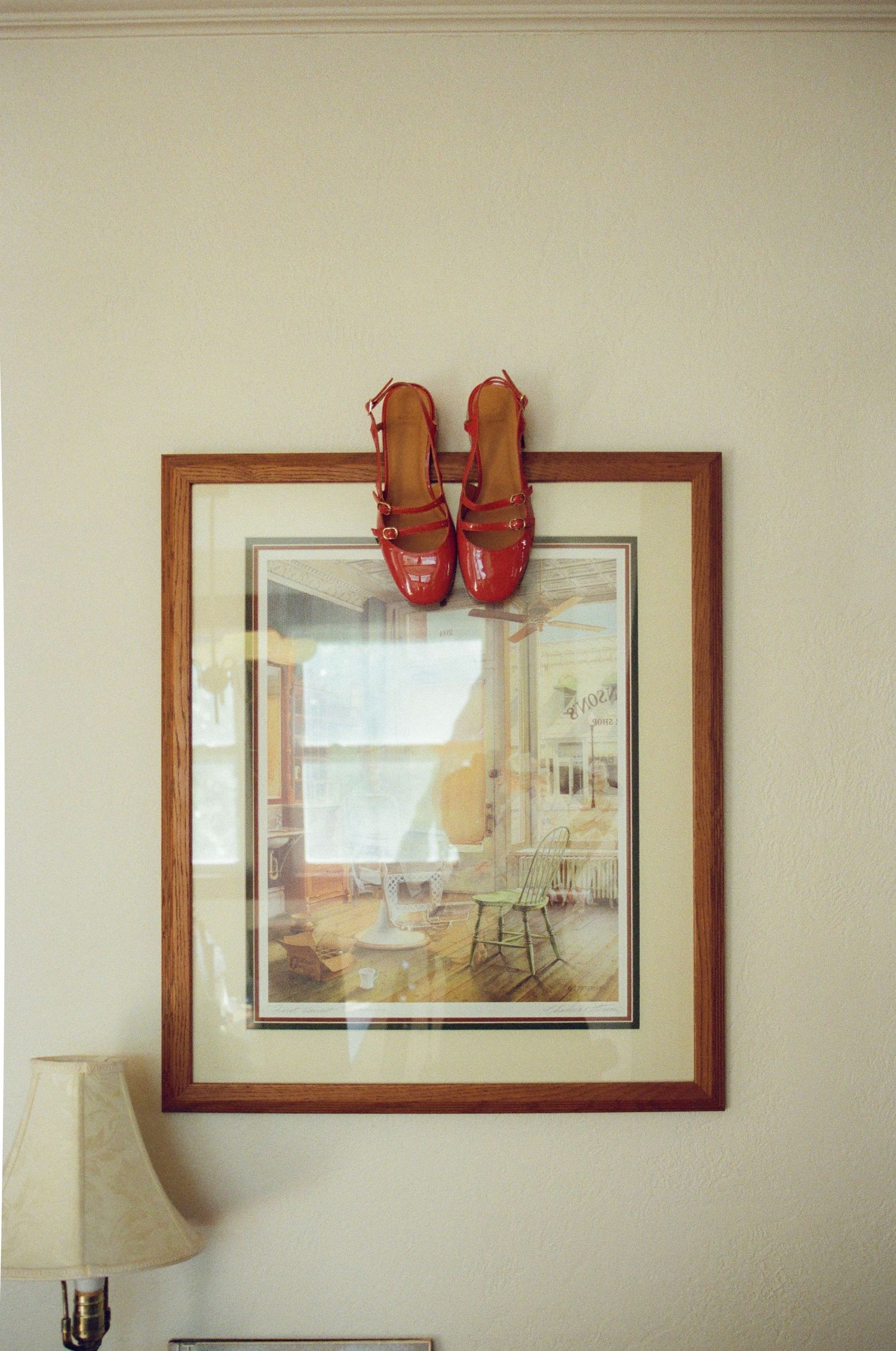 A series of framed artwork on a beige wall with small red shoes mounted above one of the frames.
