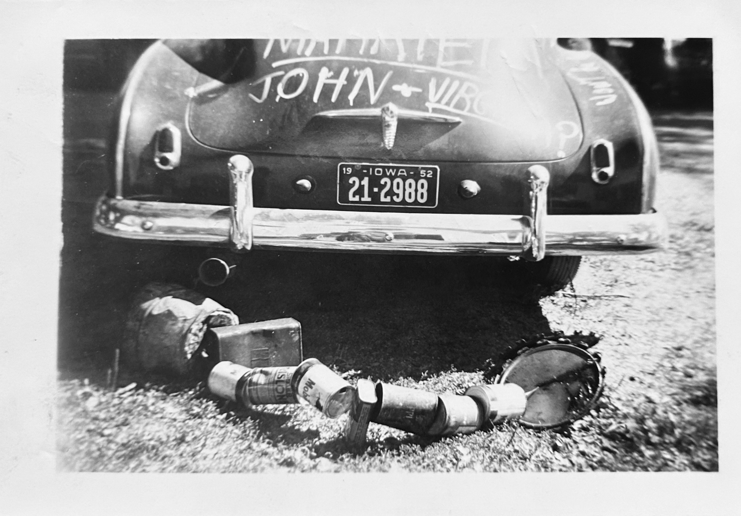 A black and white photo of a vintage hearse with ornate details parked on a dirt road.