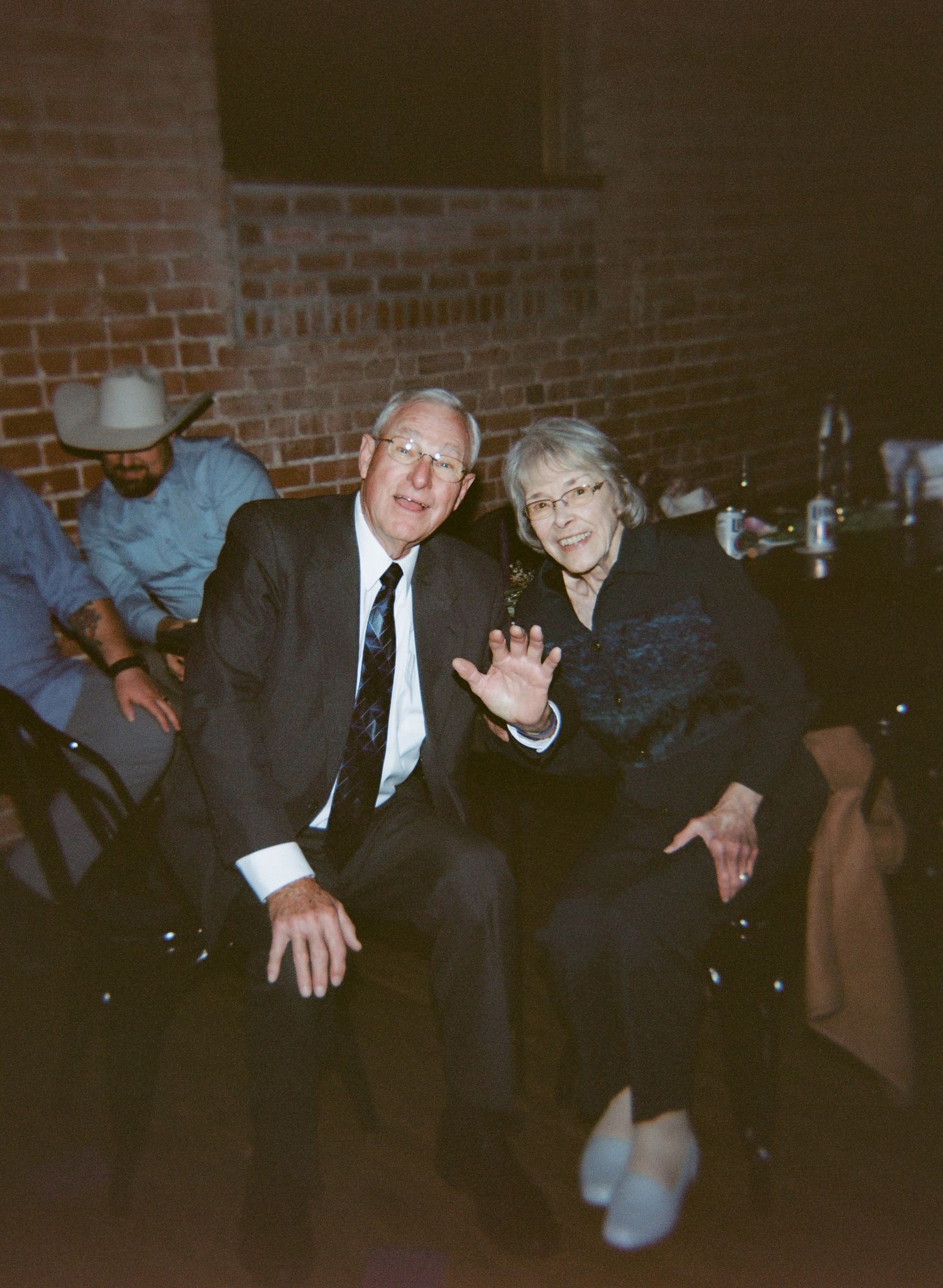 People seated at a social gathering in a dimly lit room with brick walls visible in the background.