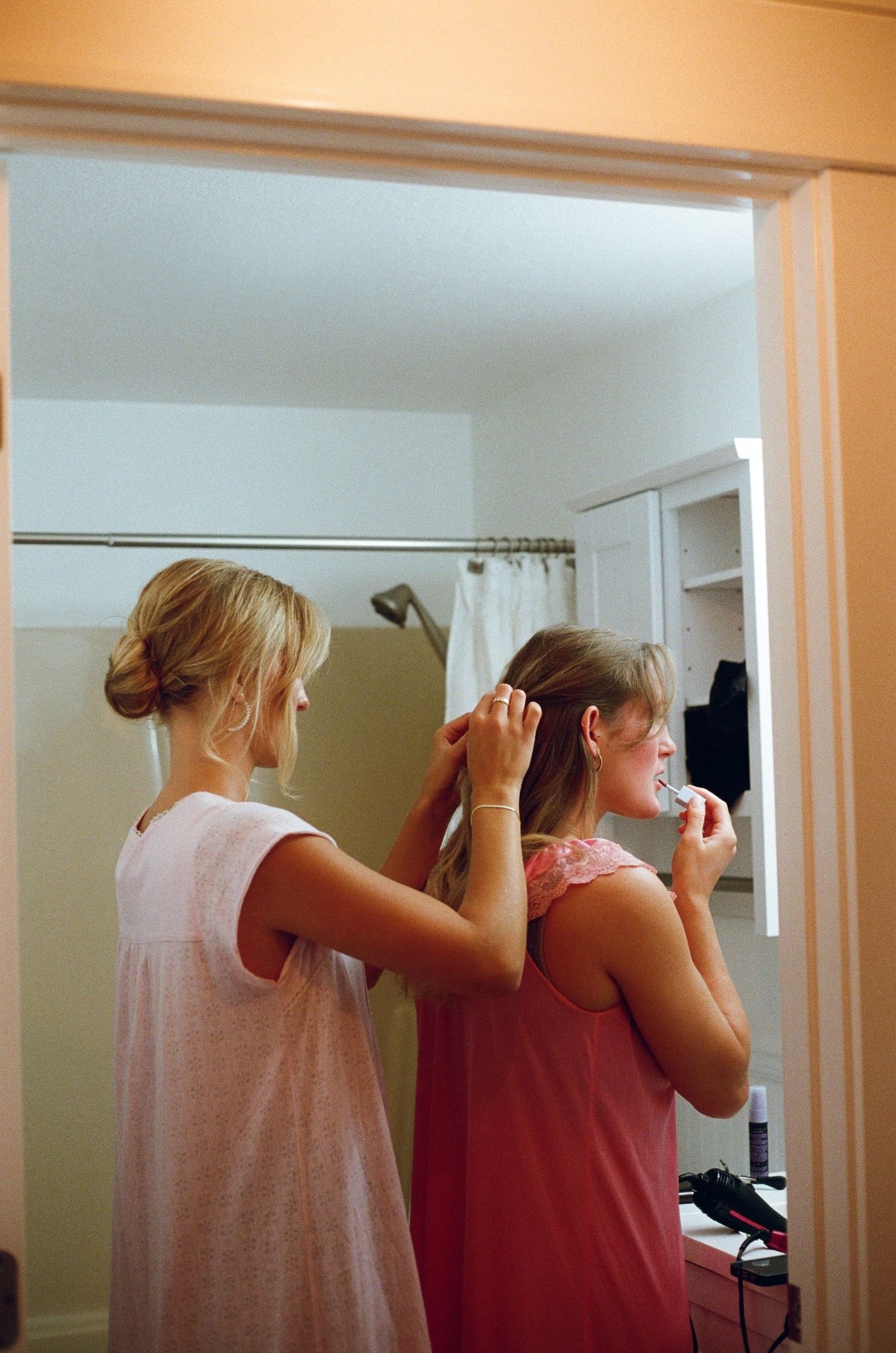 Two people getting ready in a bathroom mirror during wedding preparations.