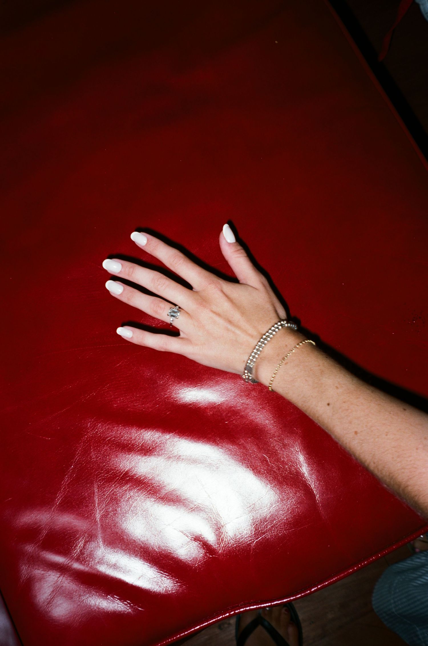 A hand adorned with rings stretches across a shiny red leather surface in a dramatic lighting setting.