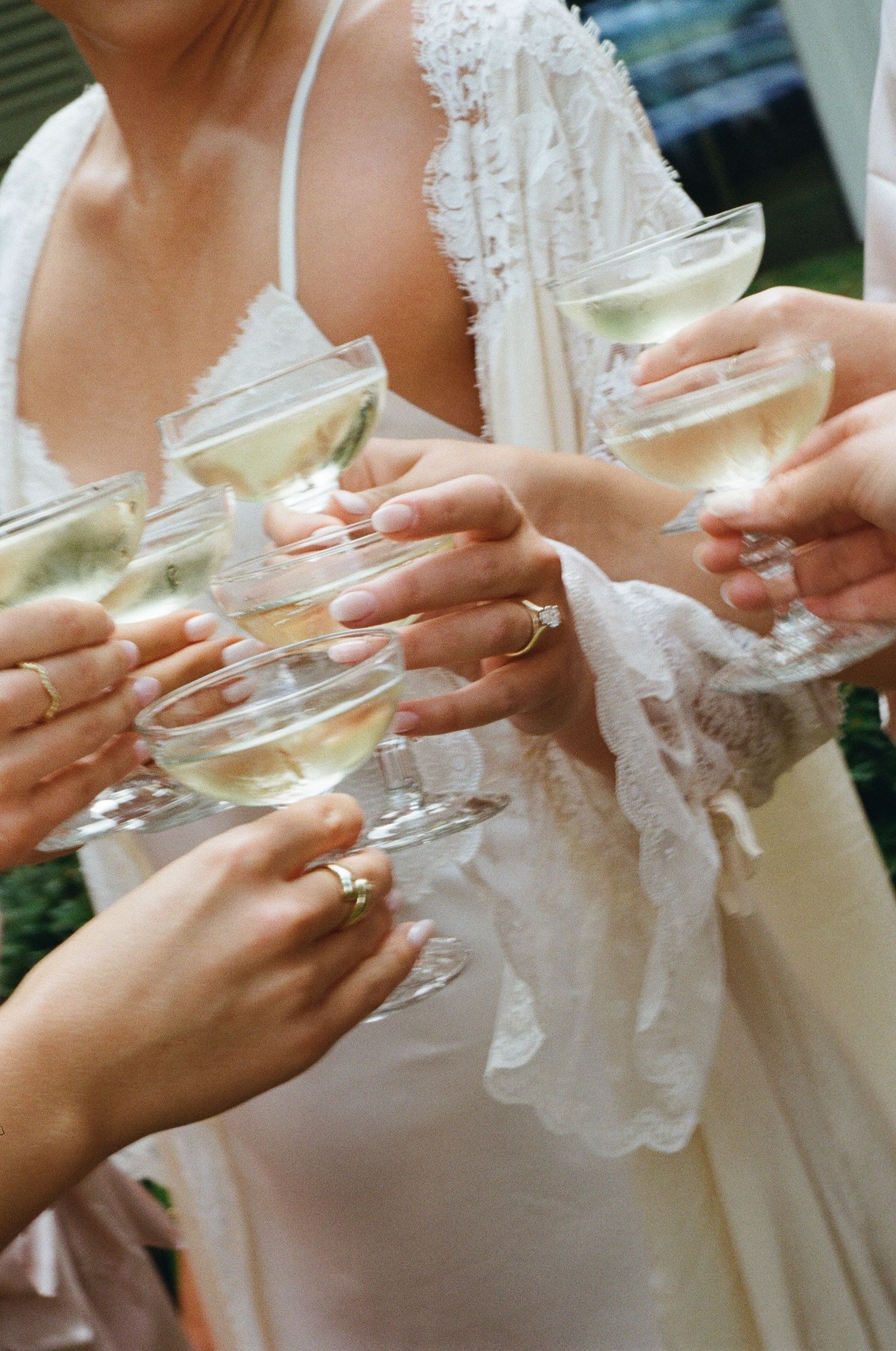 Close-up of hands holding champagne glasses showing wedding rings in delicate lace and white dress details.