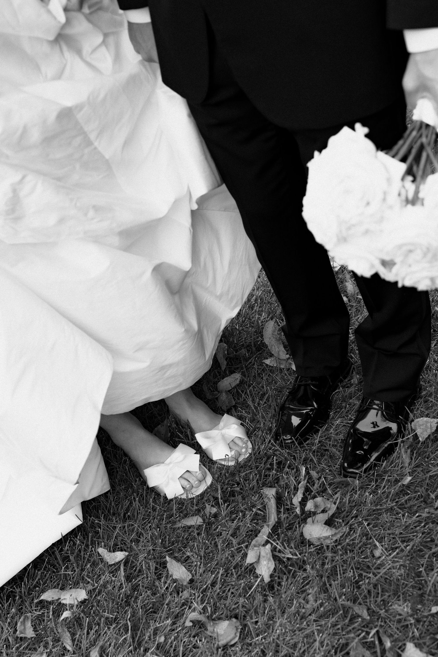 Black and white wedding photo showing dress hem and shoes of wedding party standing on grass.